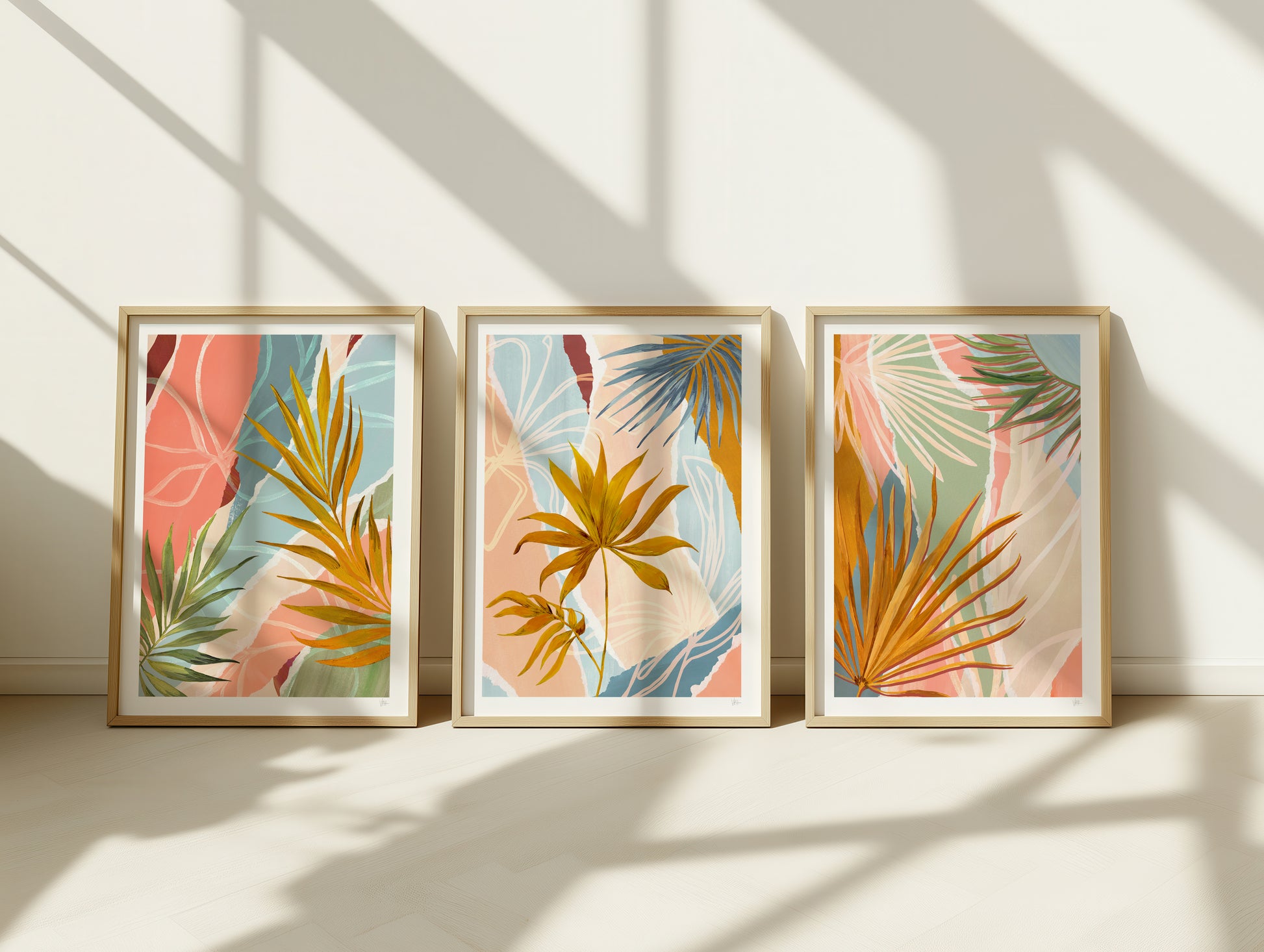 Three framed tropical leaf prints on a wall with sunlight casting shadows.