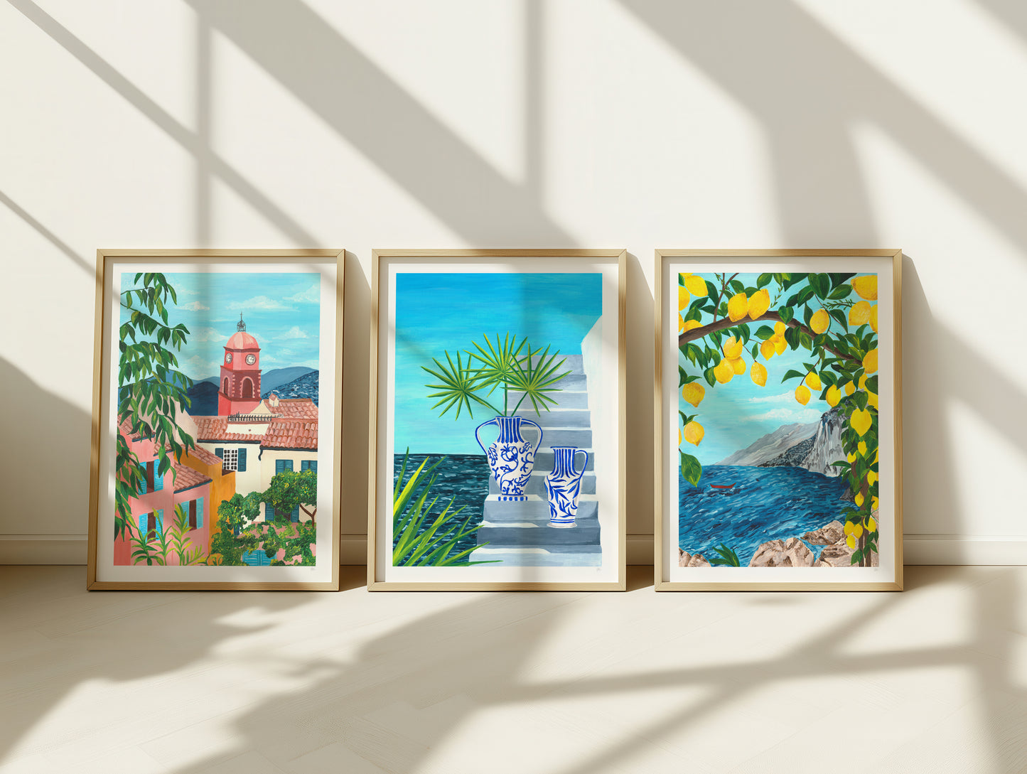 Three framed artworks on a wall with sunlight casting shadows.