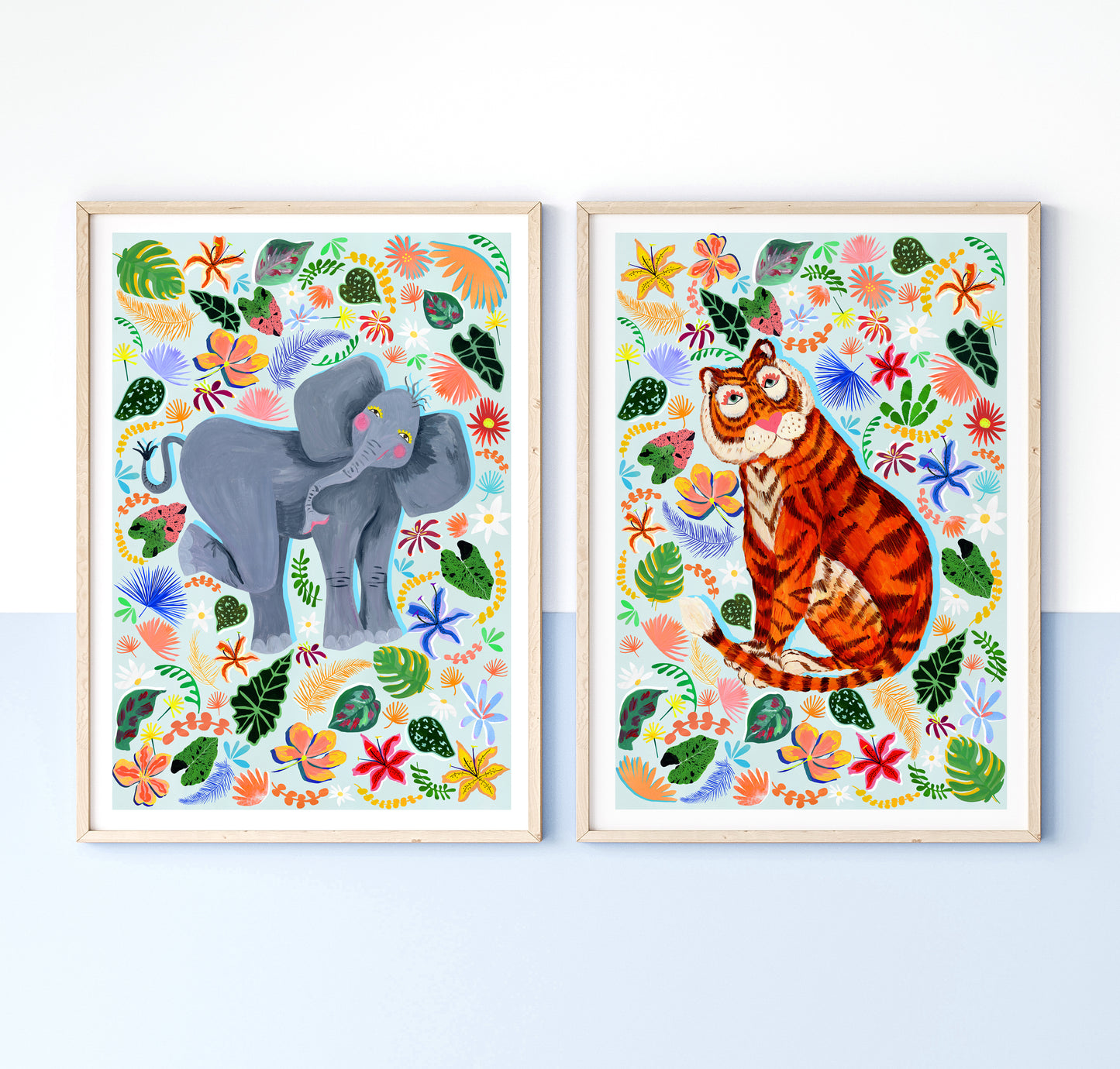 Two framed illustrations of an elephant and a tiger surrounded by colorful floral and leaf patterns on a white background.