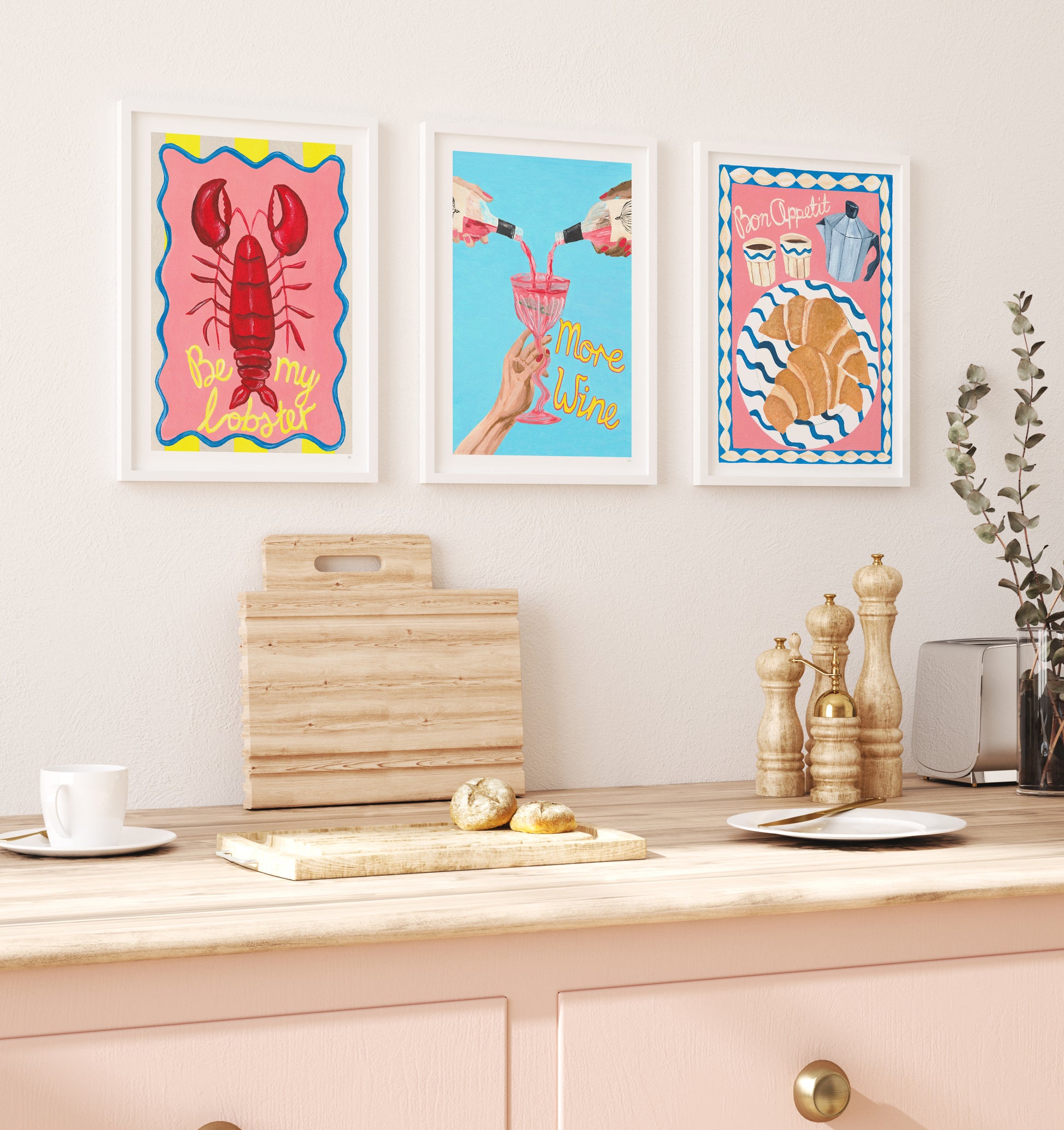 Colorful wall art prints on a kitchen wall with a cutting board and kitchen items below.