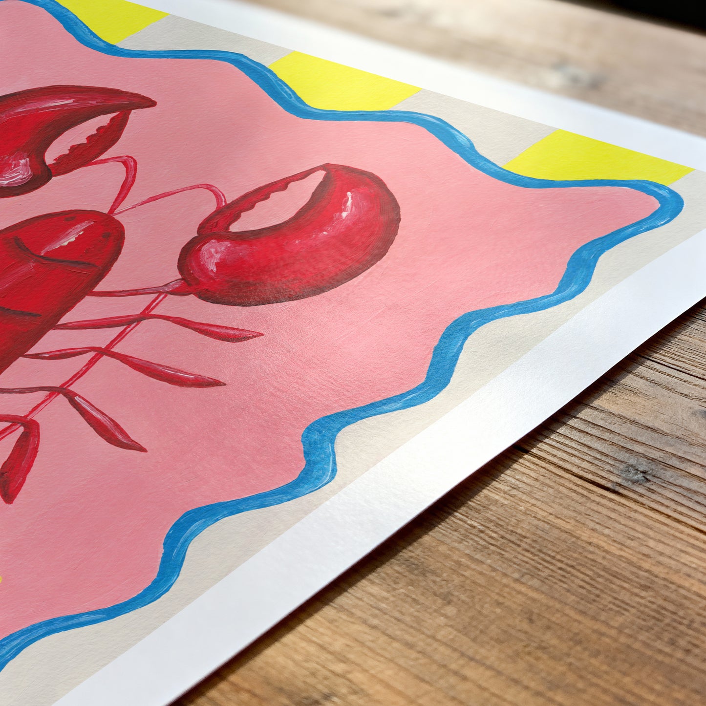 Colorful illustration of a red lobster on a pink background with blue and yellow accents, placed on a wooden surface.