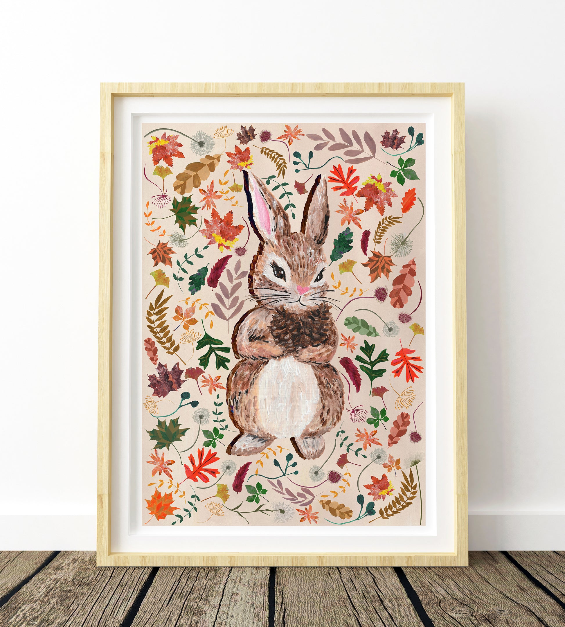 Framed artwork of a rabbit surrounded by autumn leaves on a wooden floor.