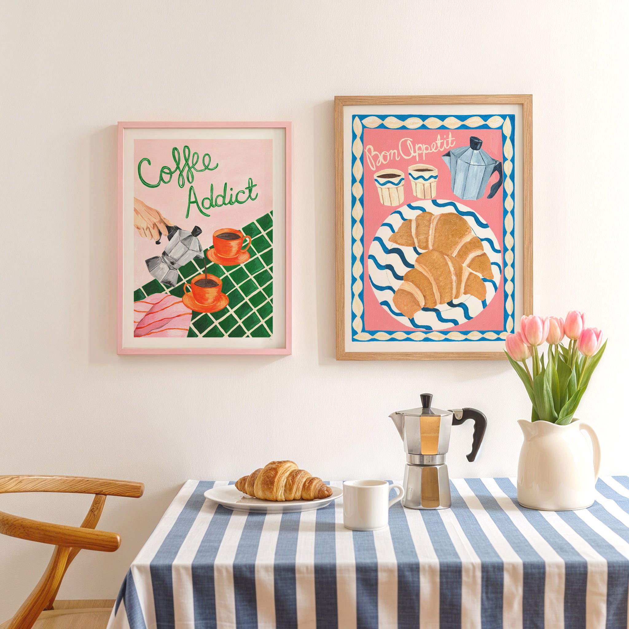 A breakfast table with blue and white striped tablecloth with breafast of the table displaying 2 hand painted retro style coffee and breakfast art prints above the table