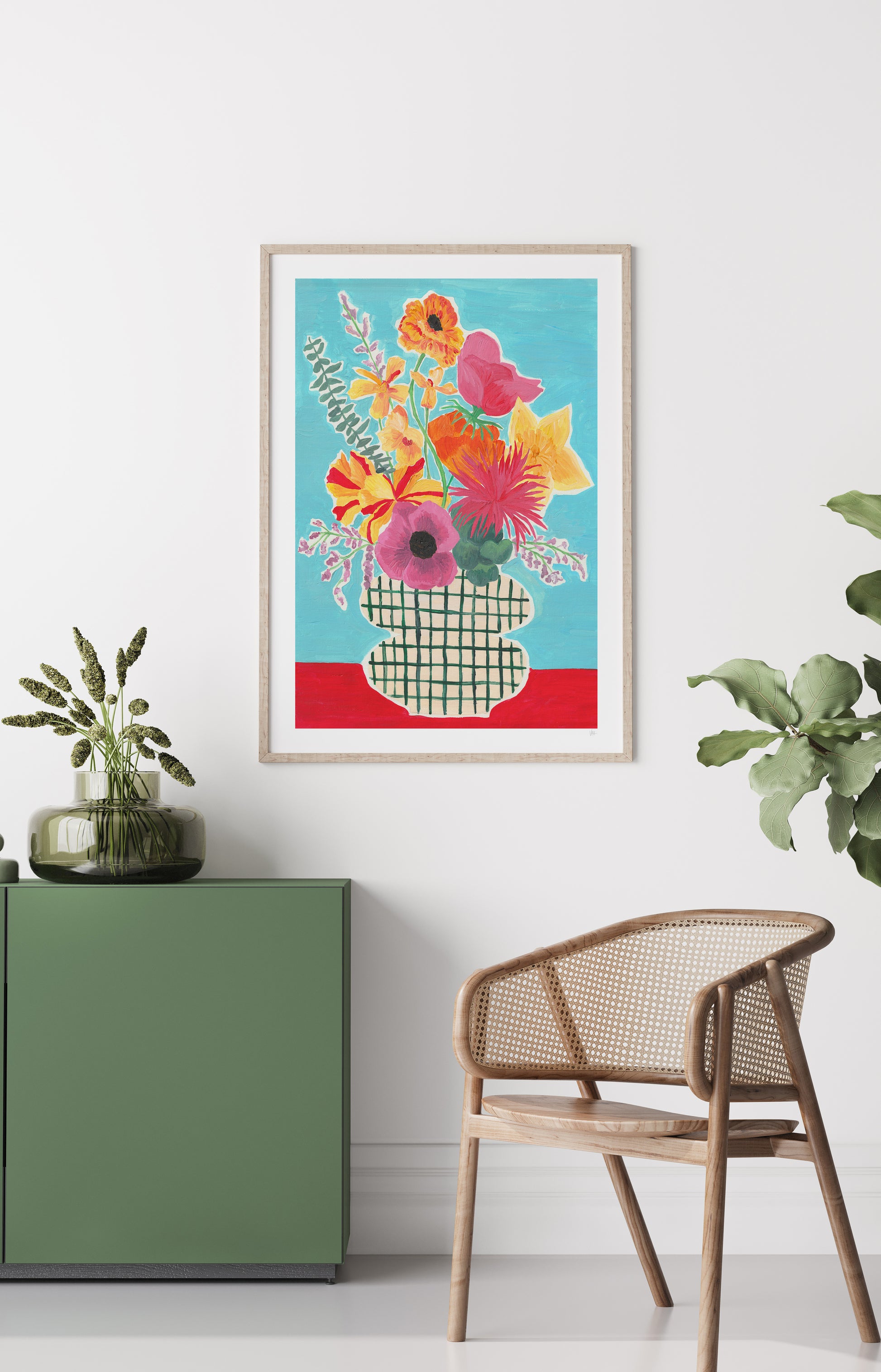 Colorful floral artwork in a frame on a white wall above a wooden chair and green cabinet.