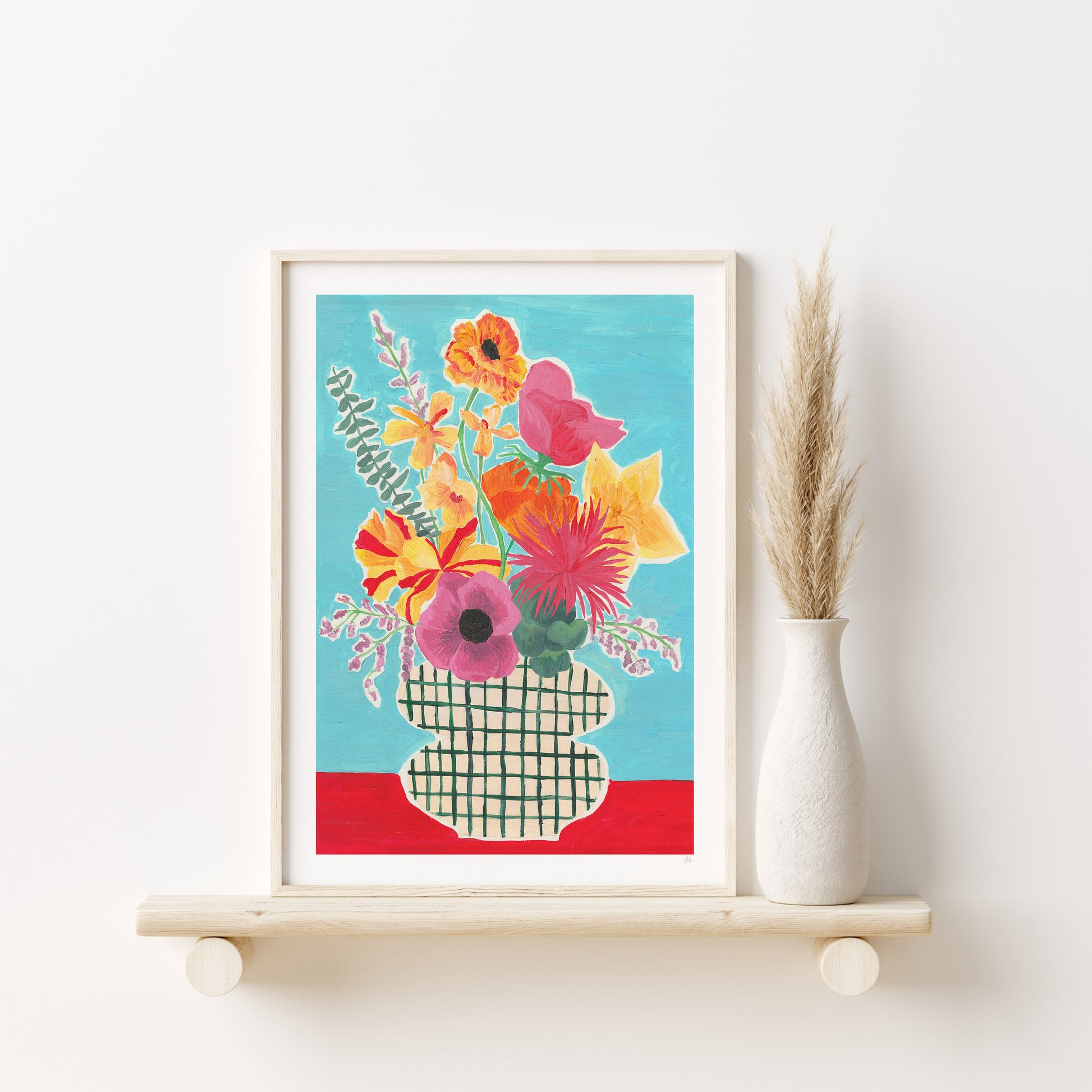 Framed floral artwork on a white wall with a vase of dried plants.