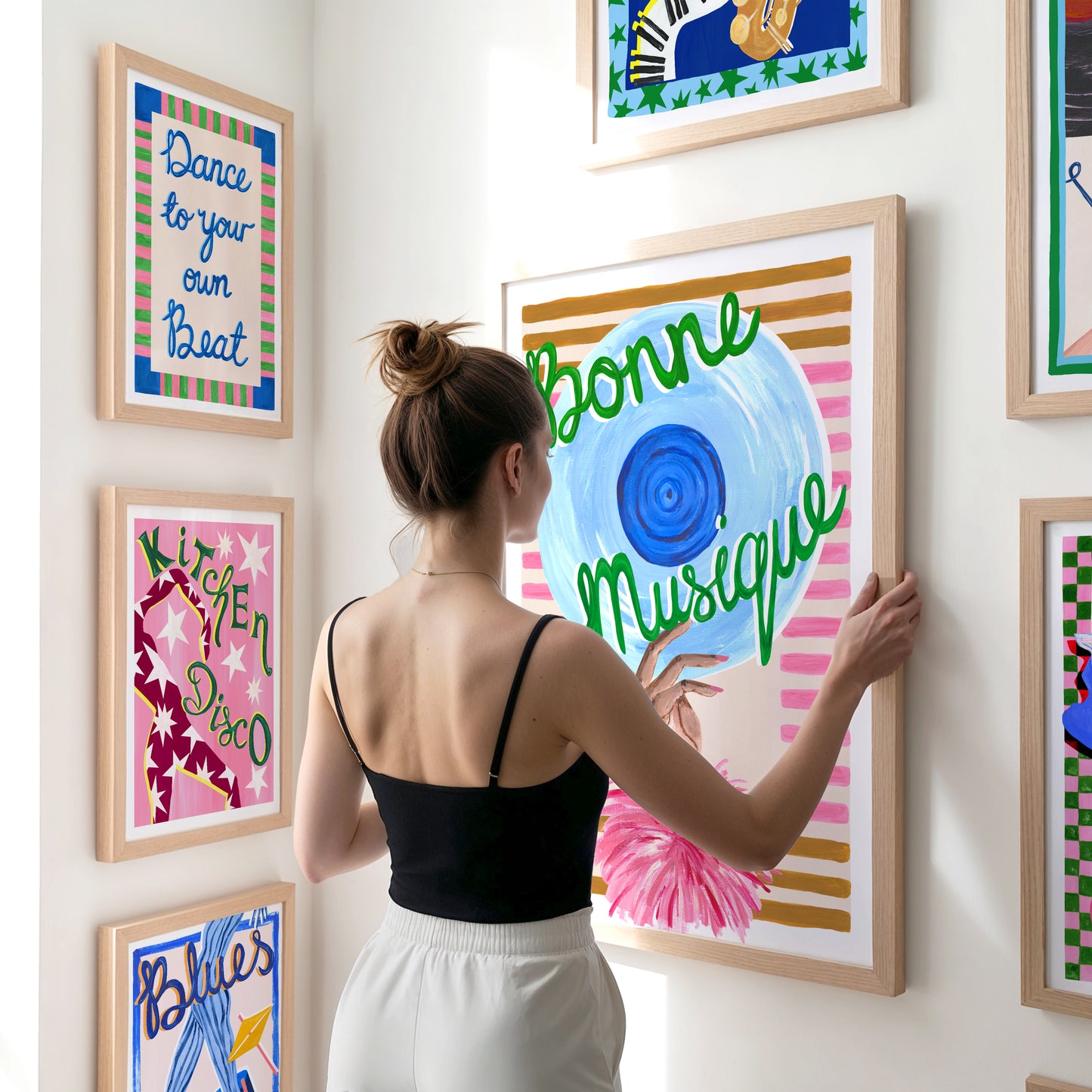 Woman arranging colorful framed artworks on a wall