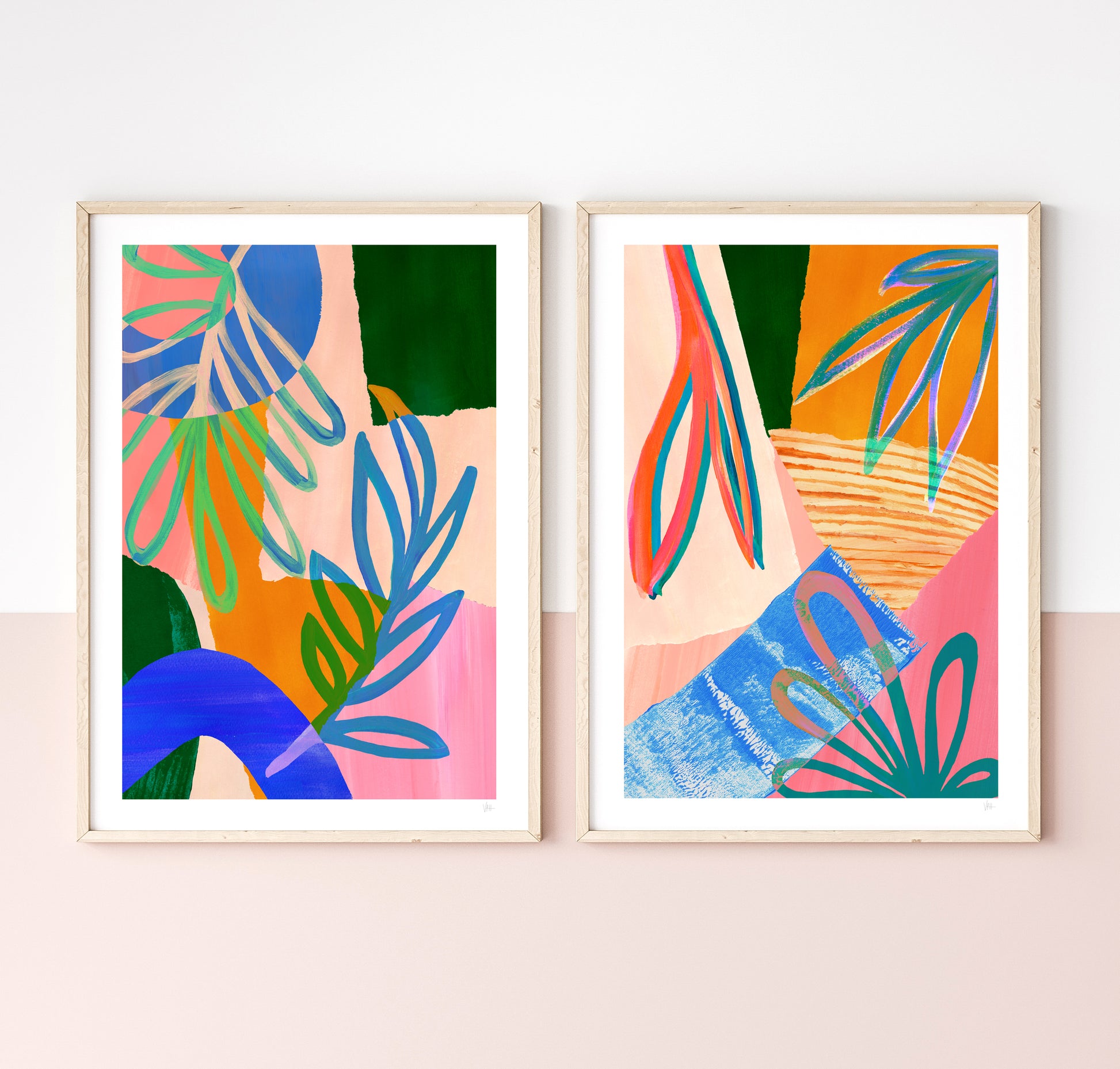 Two colorful abstract art prints in wooden frames on a light pink wall.