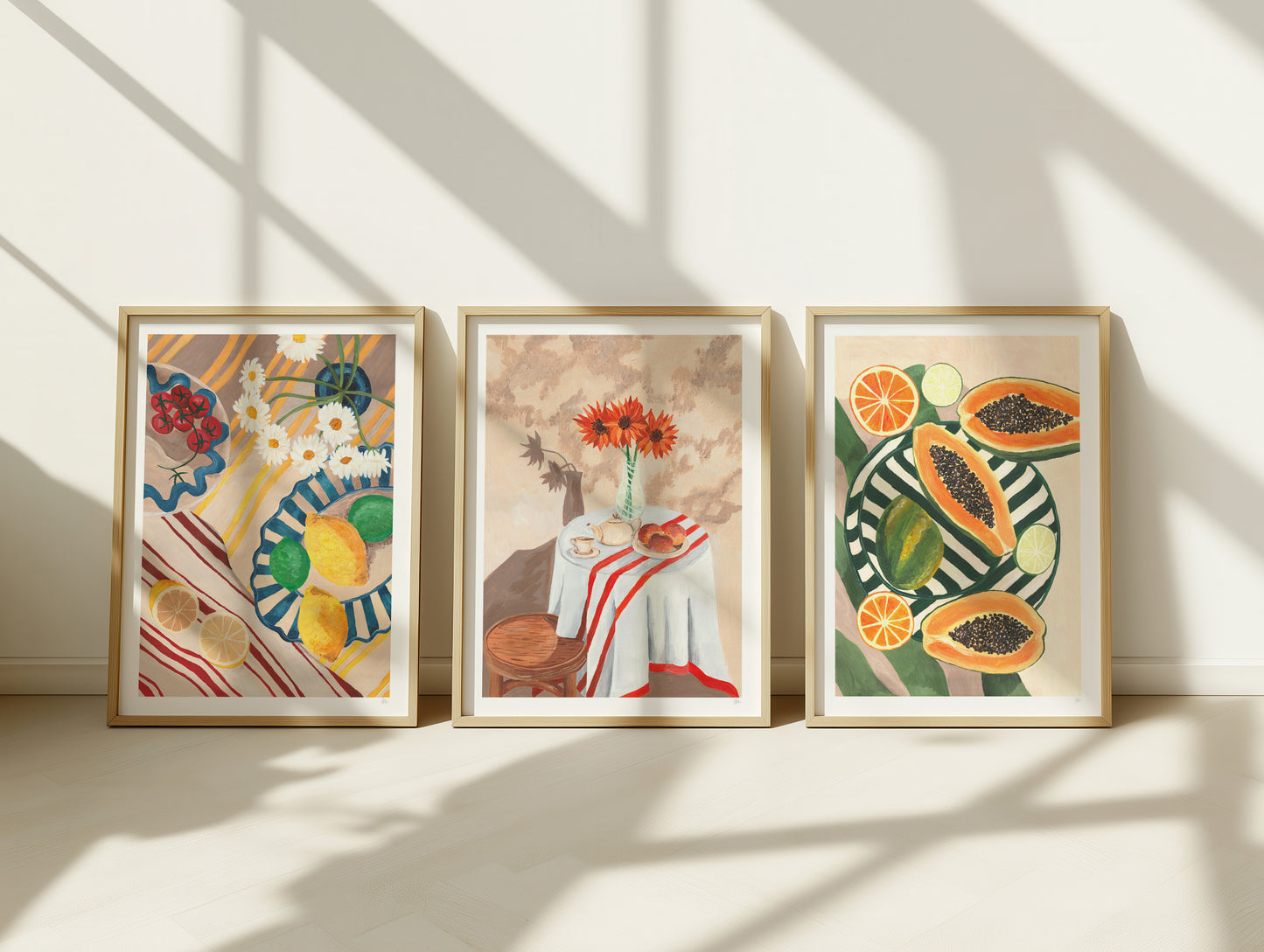 Three framed artworks on a wall with sunlight casting shadows.