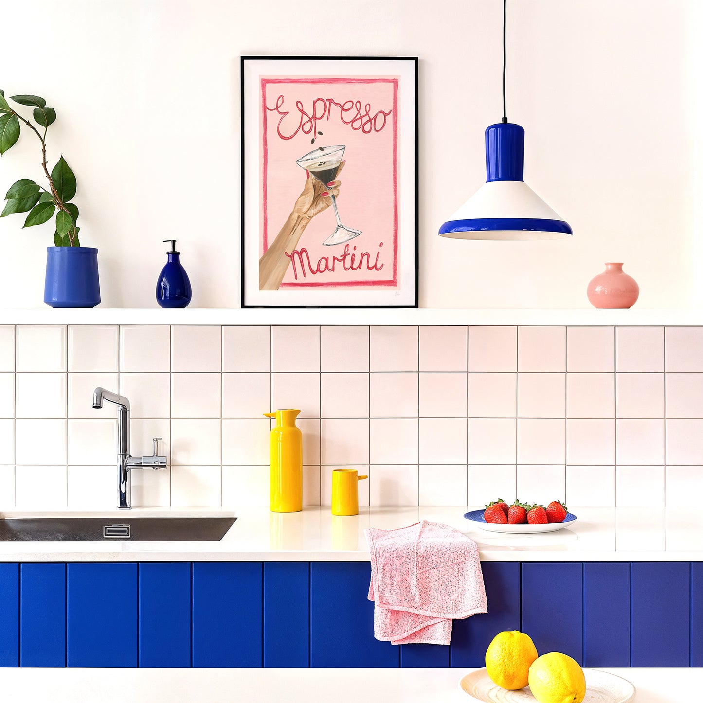 Modern kitchen with blue cabinets, white tiled backsplash, and colorful decor elements, displaying a pink espresso martini cocktail print.