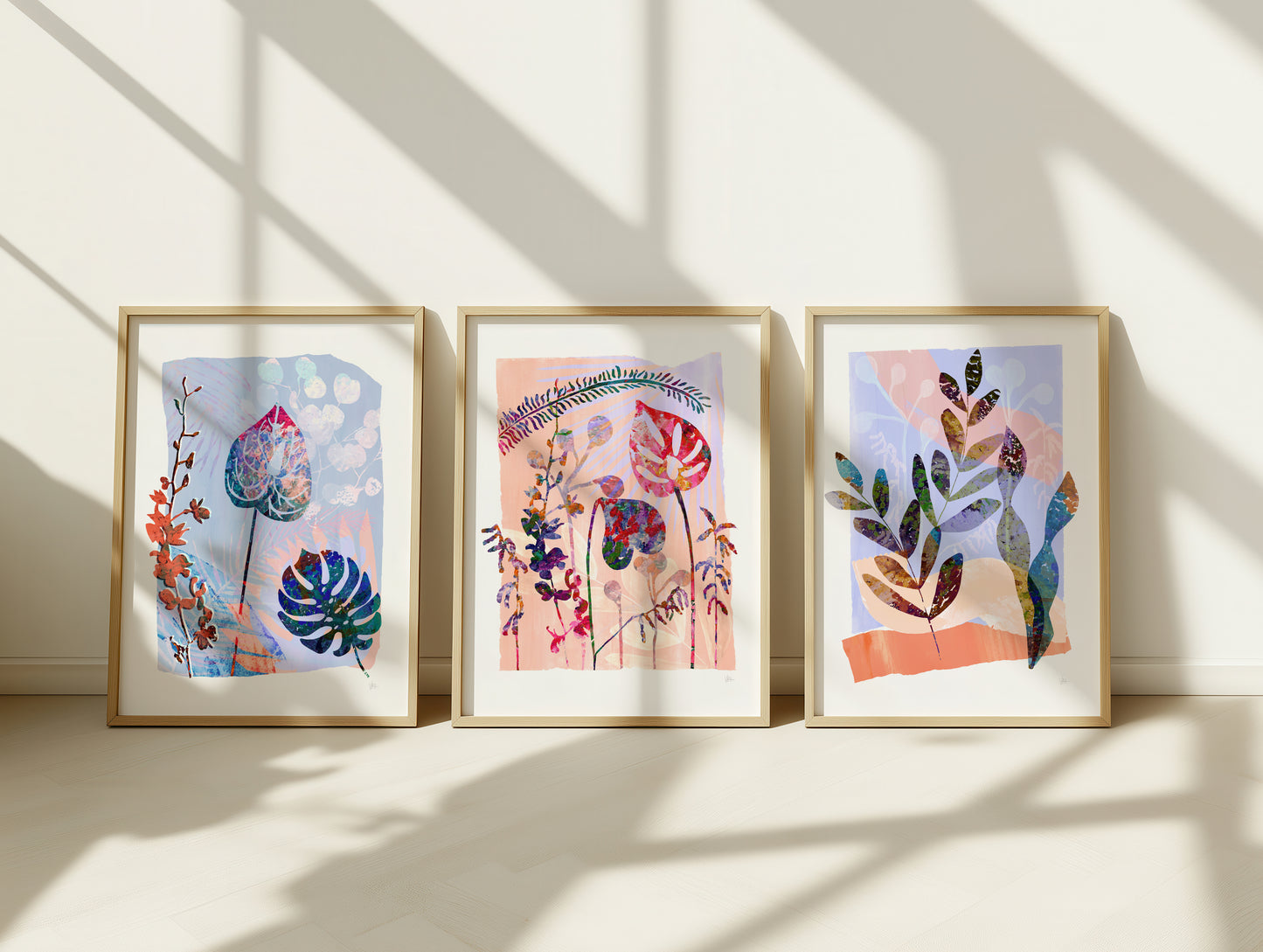 Three framed pieces of abstract art with colorful plant-like designs on a white wall.