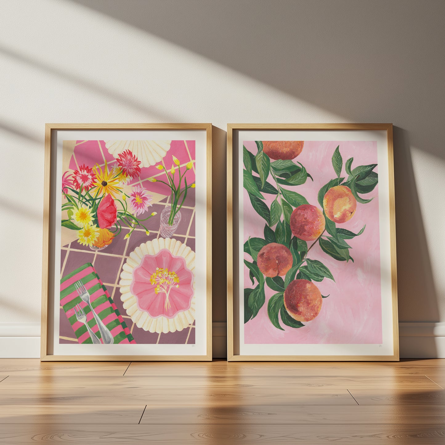 2 framed hand painted prints of a picnic scenne dispaying flower on a check pink tablecloth and leafy green peaches on a pale pink background