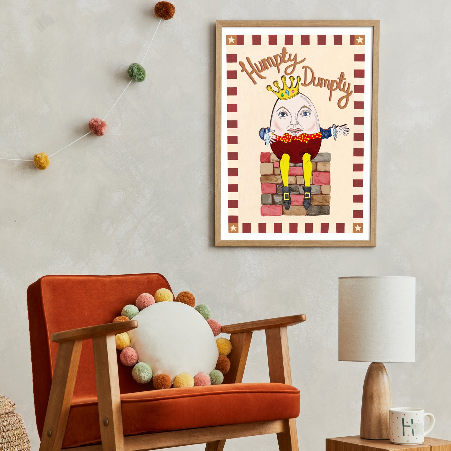 Framed artwork of Humpty Dumpty on a wall above an orange chair with decorative pillows.