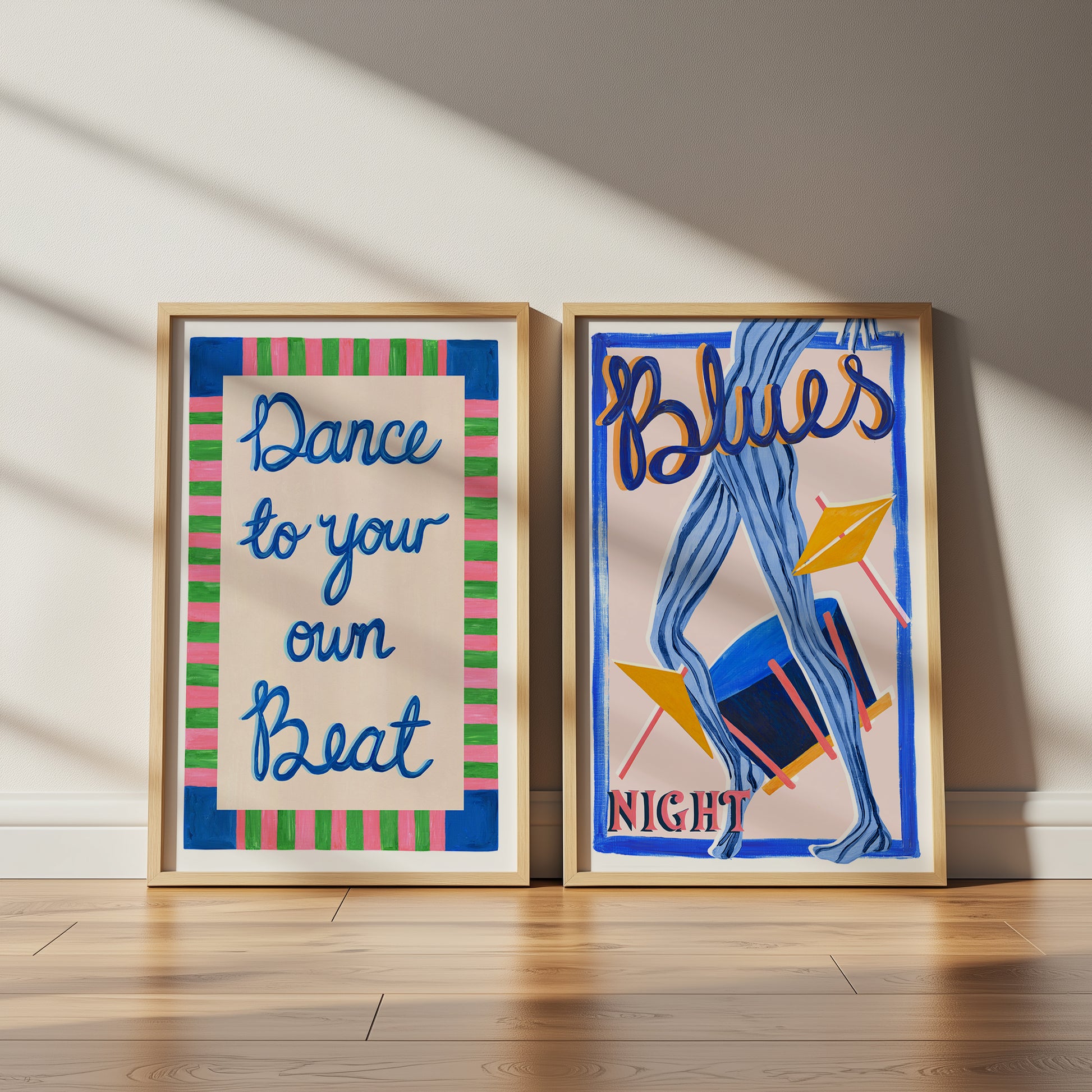 Two framed posters on a wooden floor with a neutral wall background