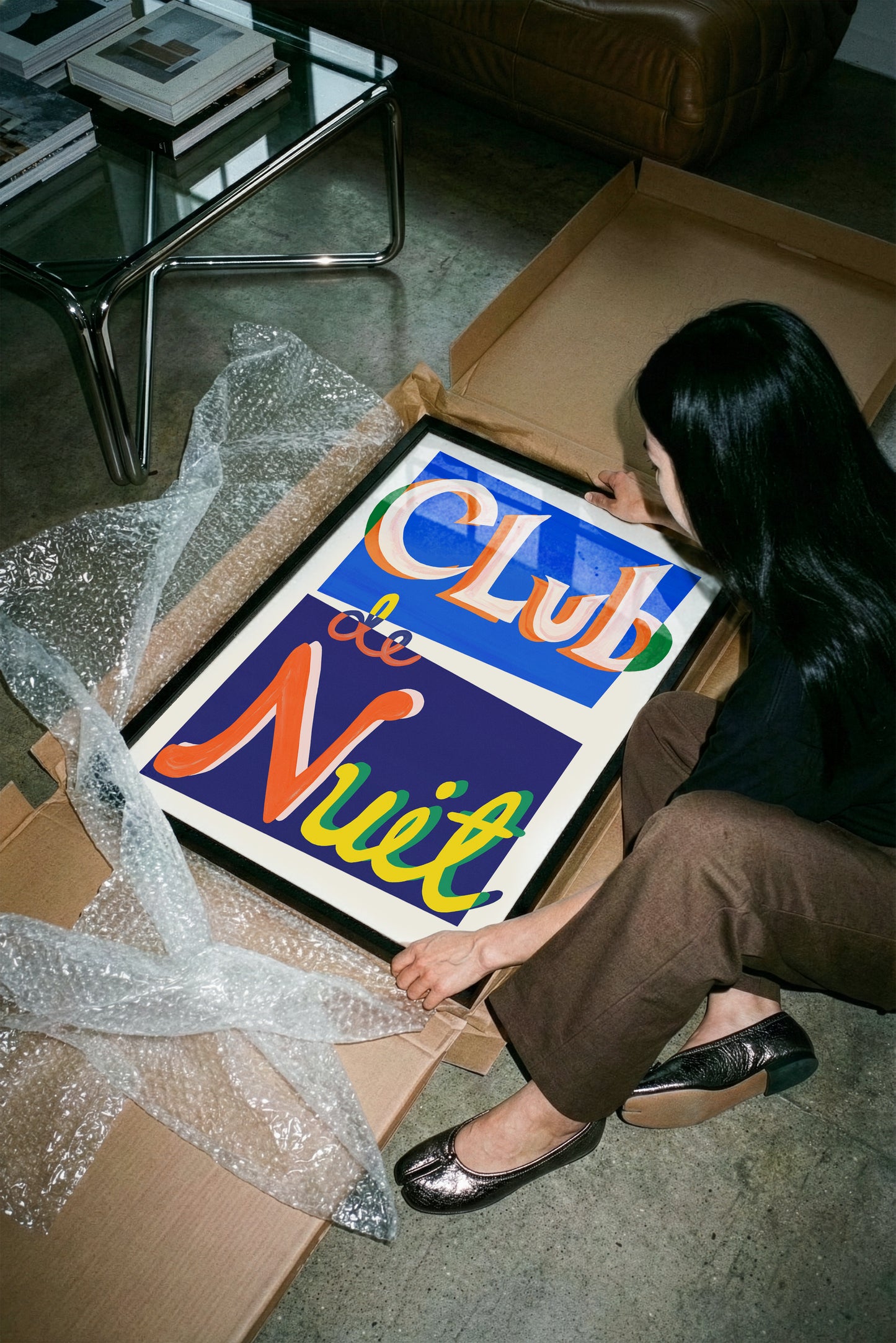 Person opening a box with a colorful sign reading 'Club de Nuit' in a room.