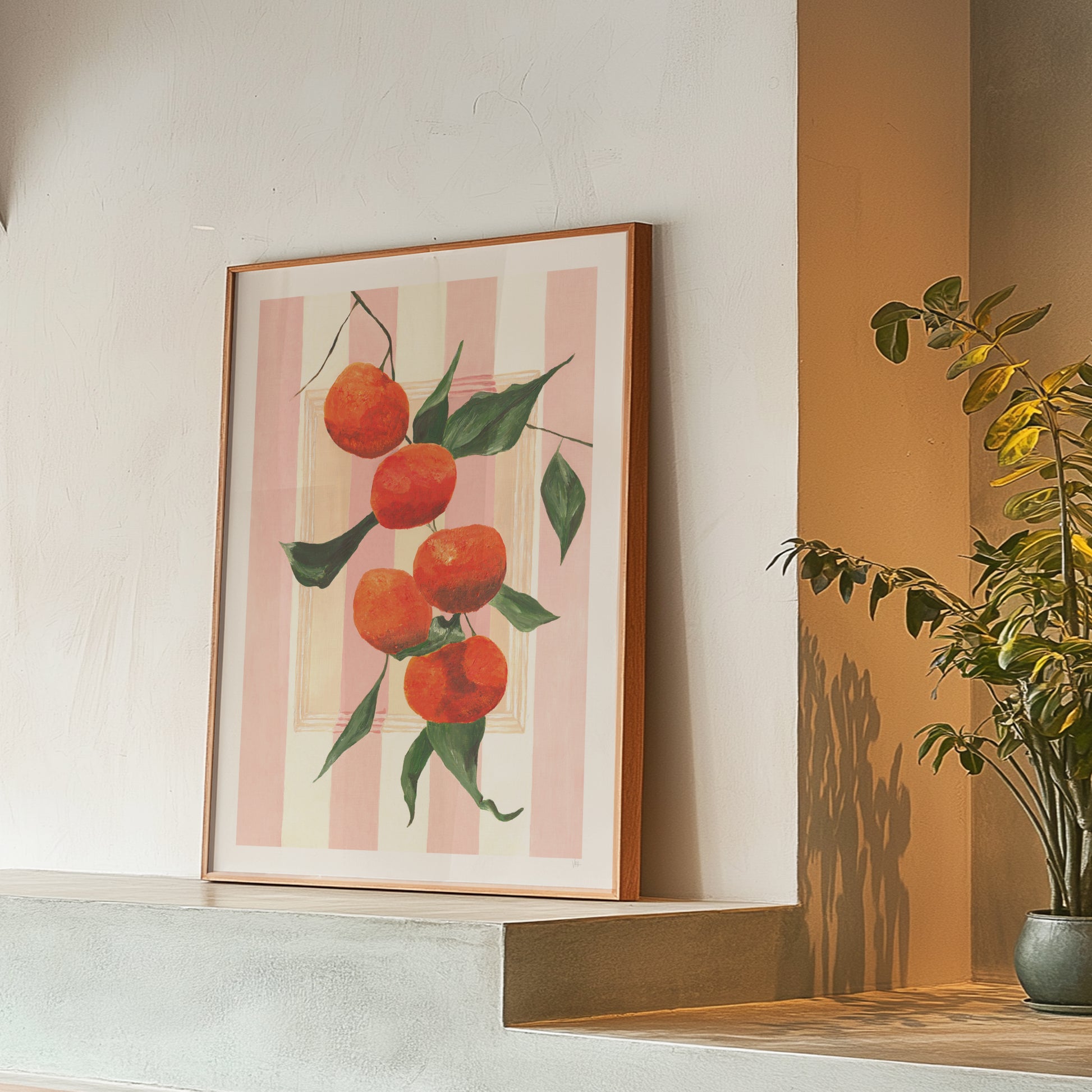 Framed artwork of oranges on a striped background hanging on a wall.