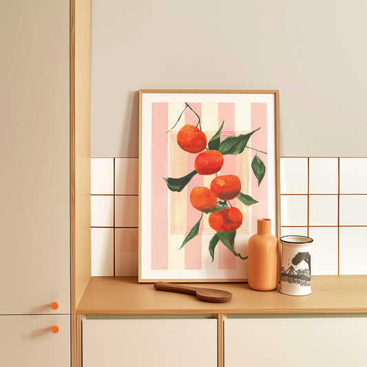 Framed artwork of tangerines on a kitchen counter with a vase and mug.