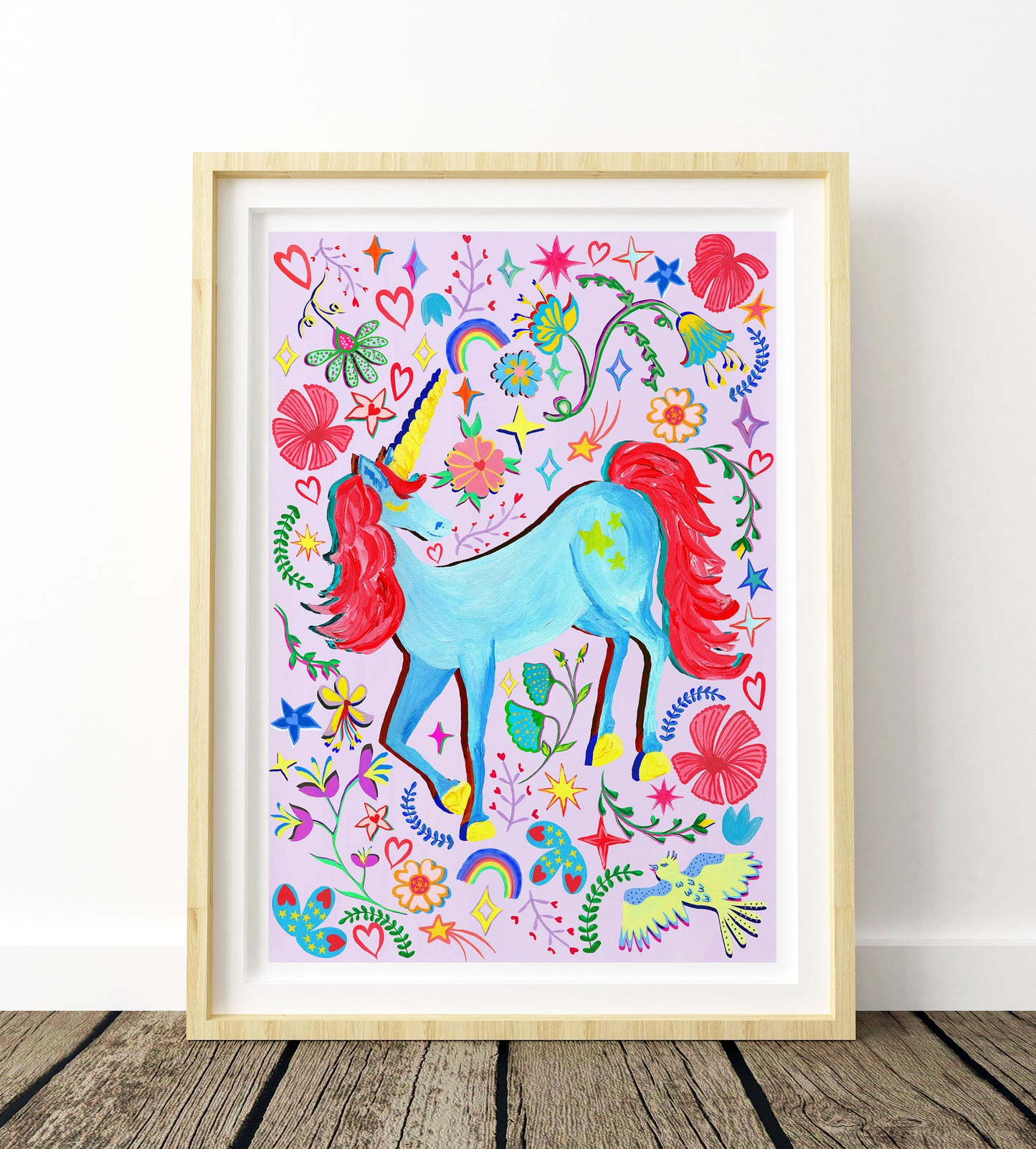 Colorful unicorn illustration with flowers and stars in a wooden frame on a white wall.