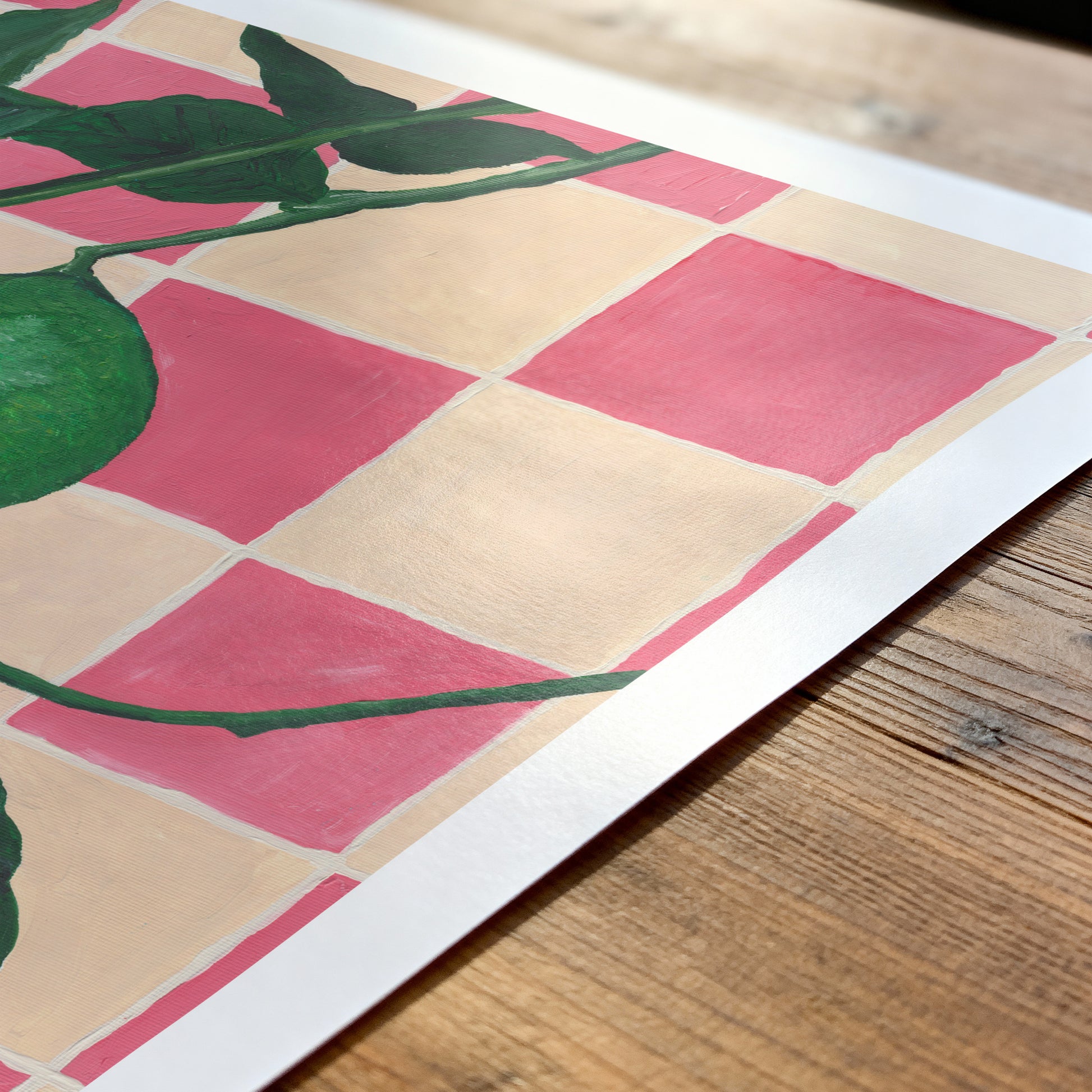 Art print of limes on a pink and cream checkered pattern background on a wooden surface