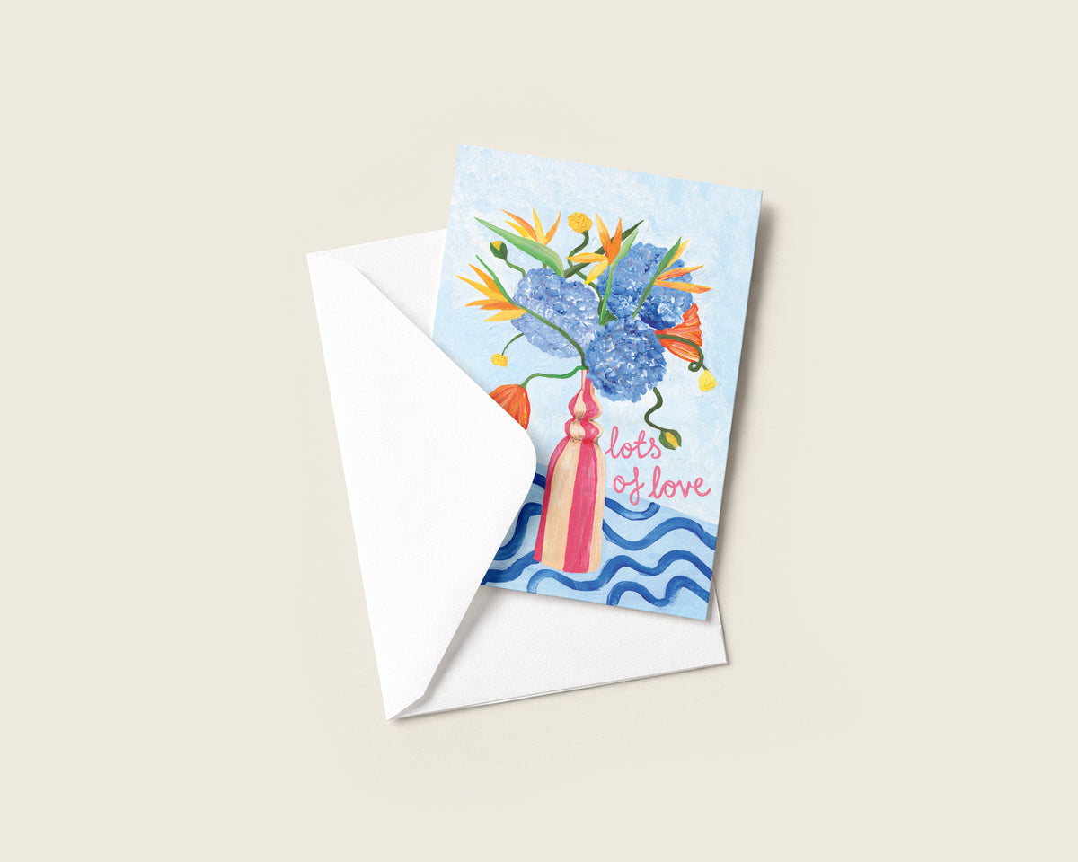 A square greeting card with a white envelope, featuring a colorful illustration of a bouquet in a pink vase with the words 'lots of love' on a light beige background.