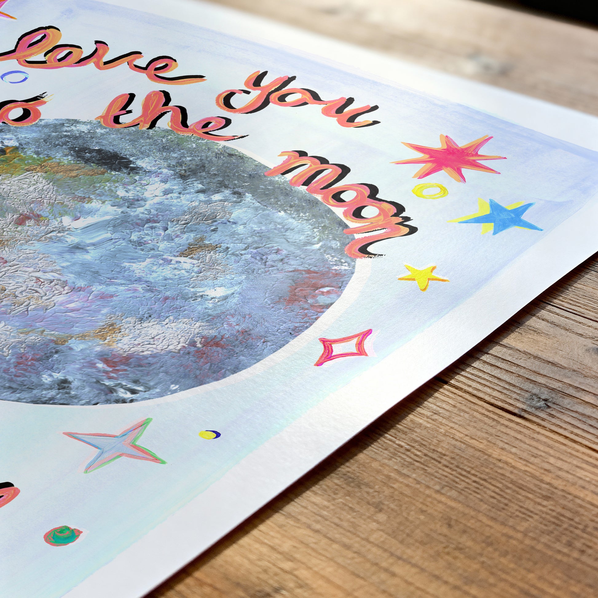 Card with 'I love you to the moon' text and colorful stars on a wooden surface