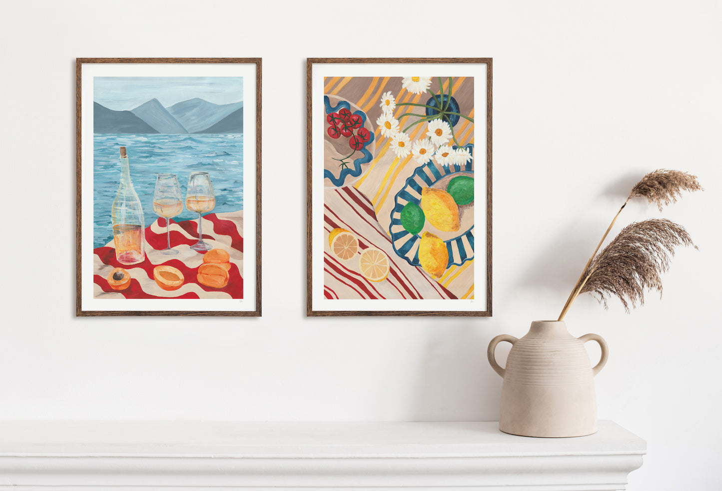 Two framed food and drink artworks on a white wall with a vase and dried plants.