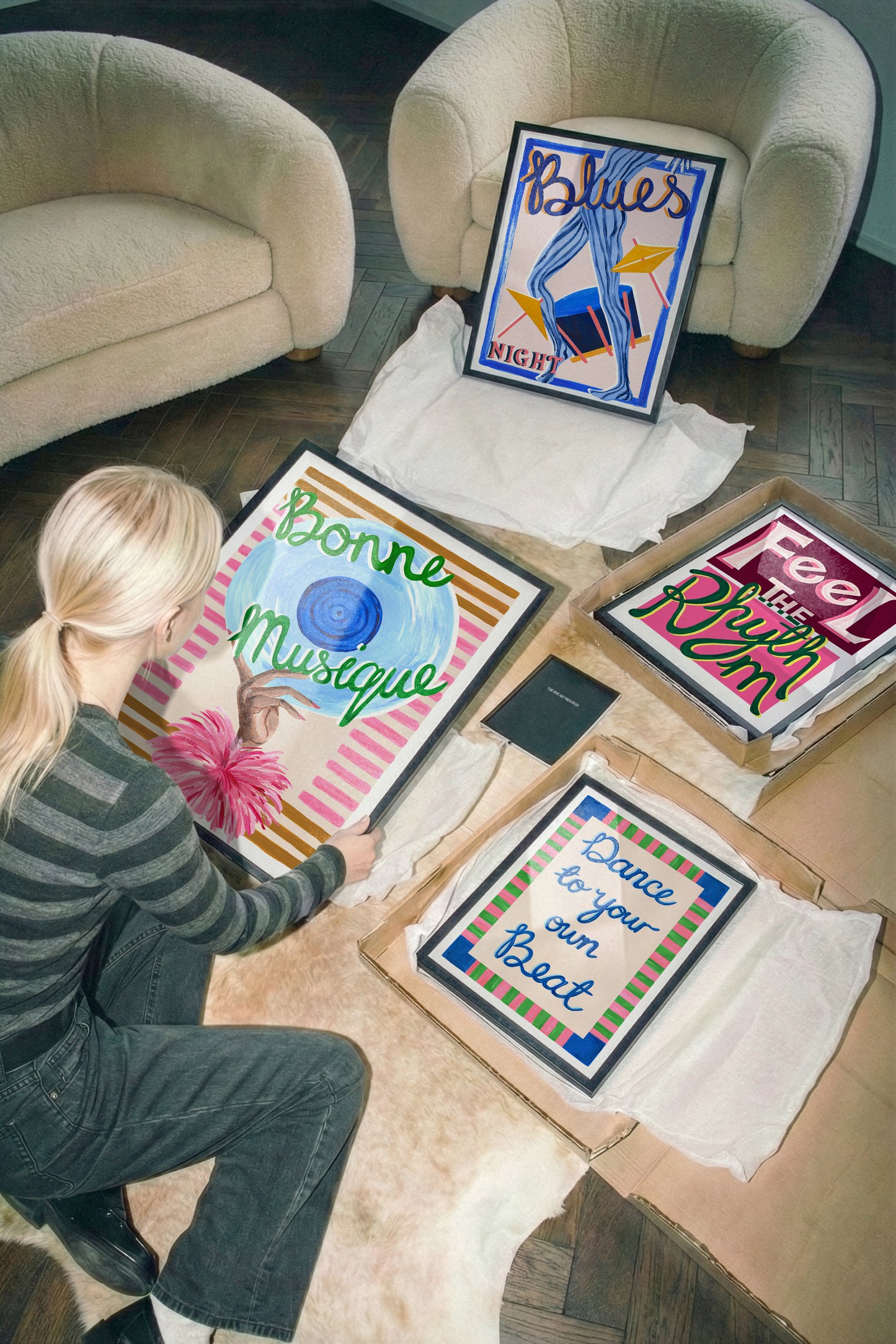 Person sitting on a couch with framed artwork on the floor.