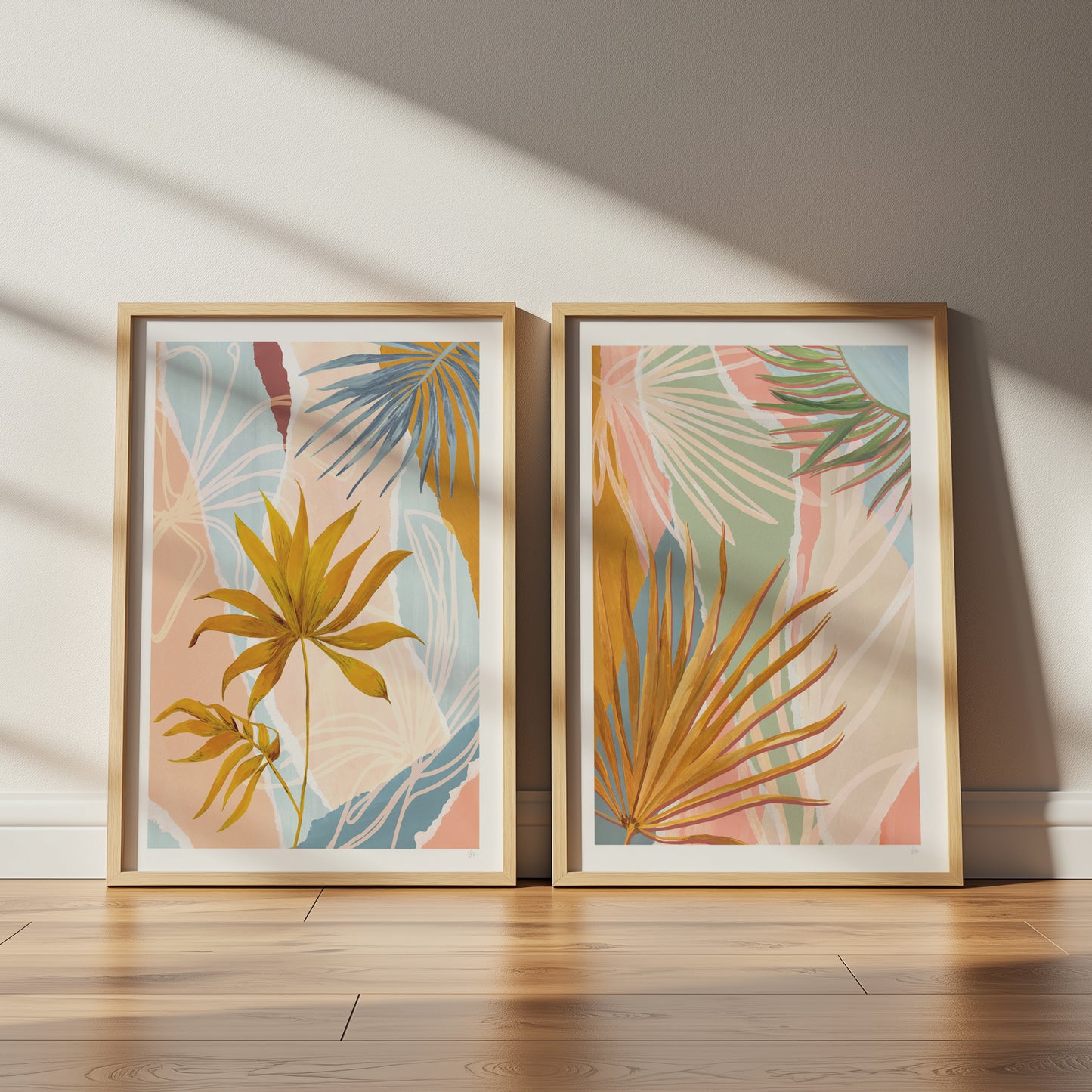 Two framed botanical prints with palm leaves on a wooden floor.
