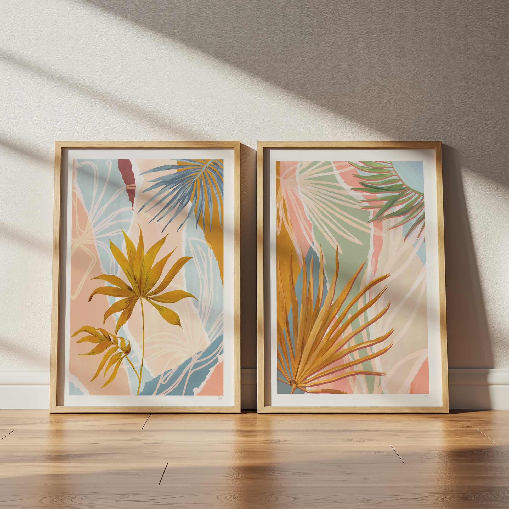 Two framed botanical prints with palm leaves on a wooden floor.