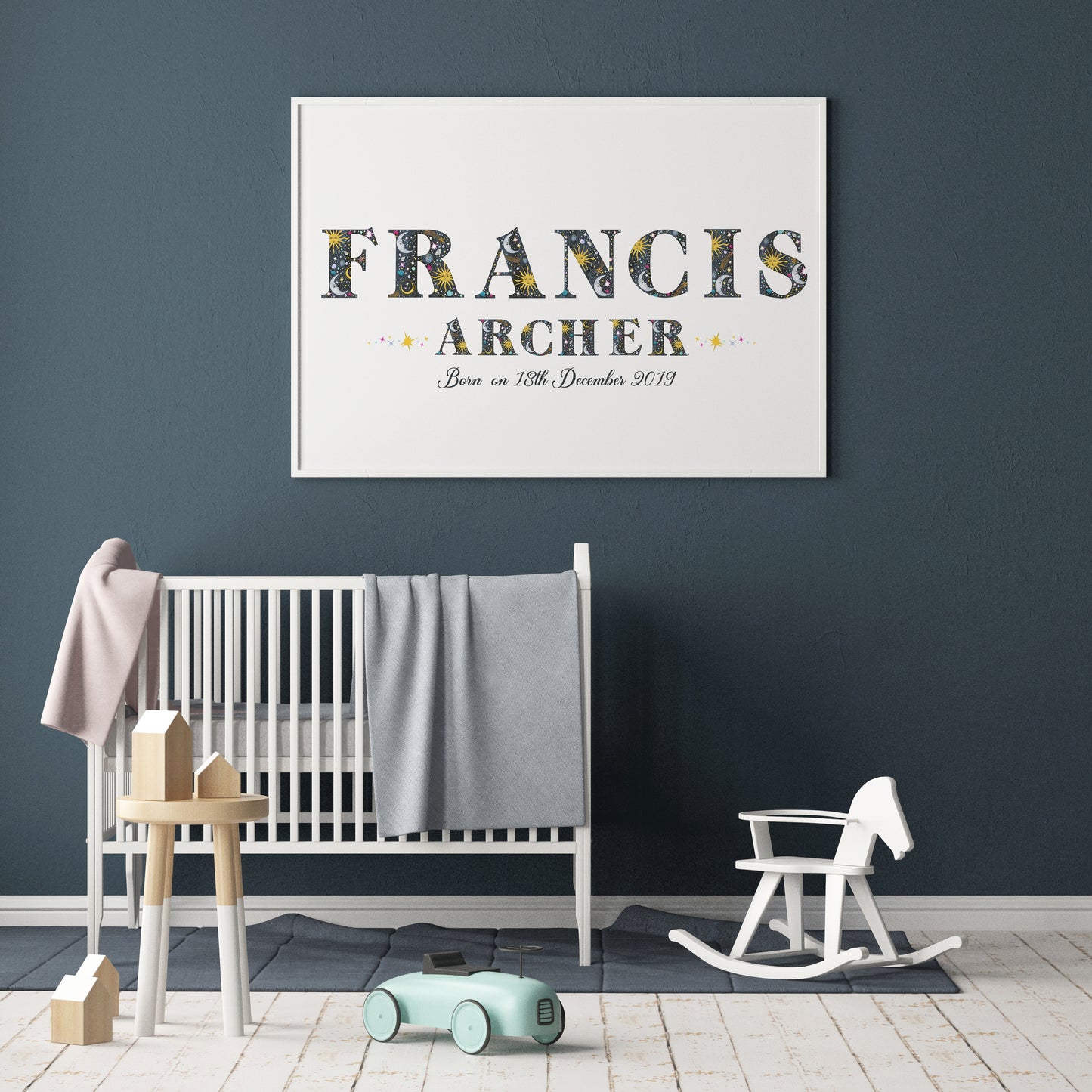 Nursery room with a crib, rocking horse, and framed name art on a dark blue wall.
