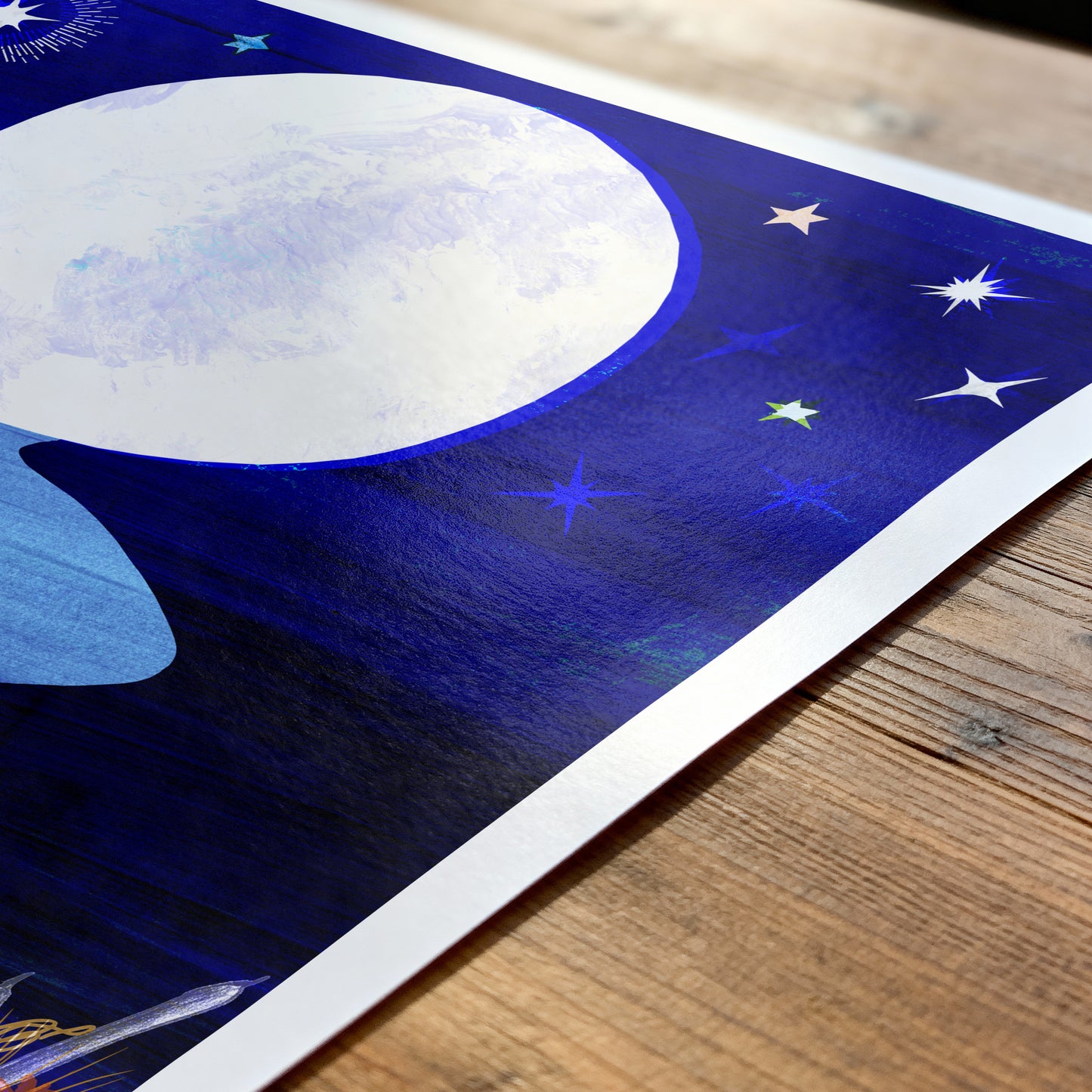 Artistic depiction of a moon and stars on a blue background, placed on a wooden surface.