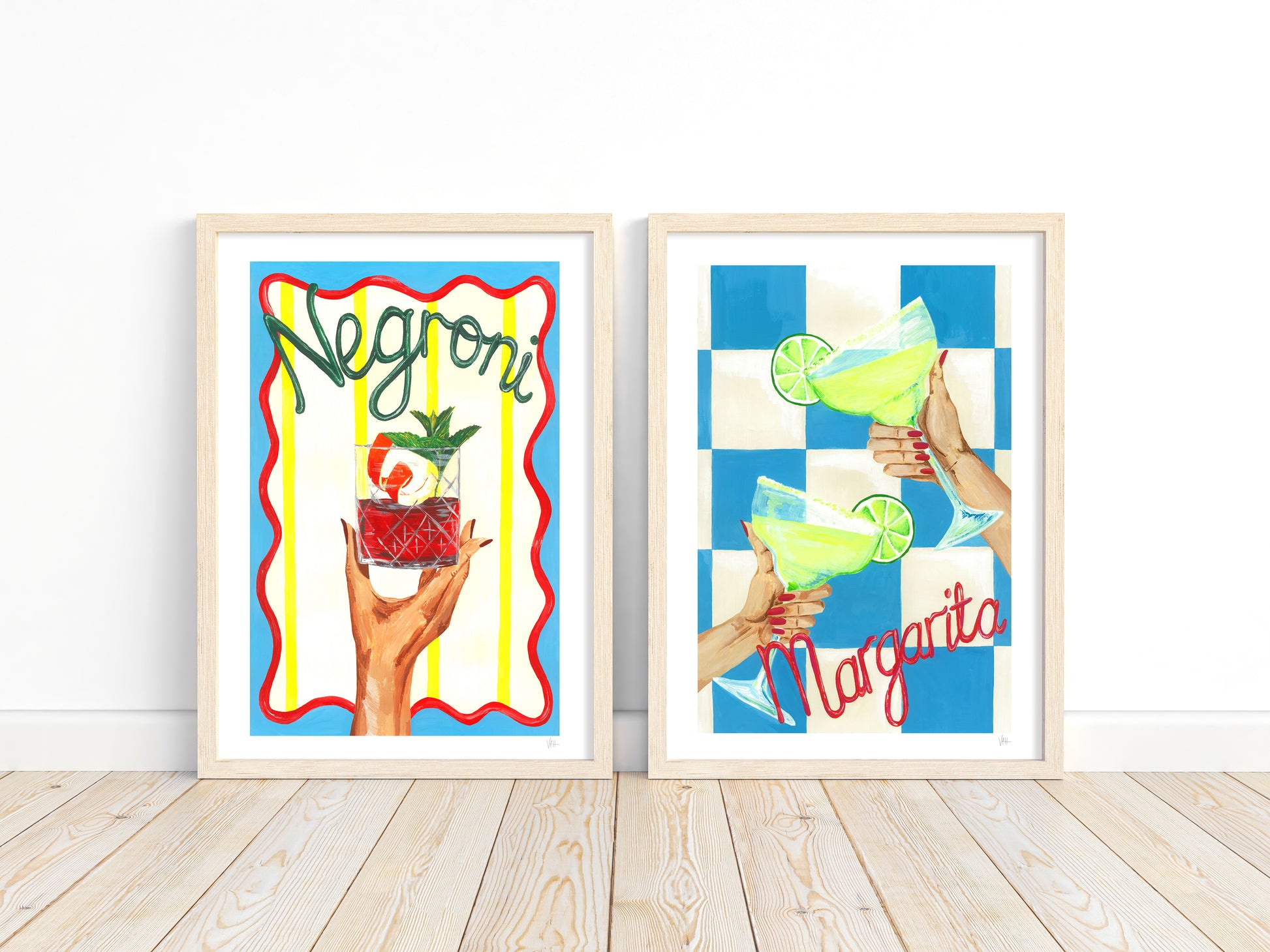 Two framed prints featuring cocktail-themed artwork on a wooden floor.