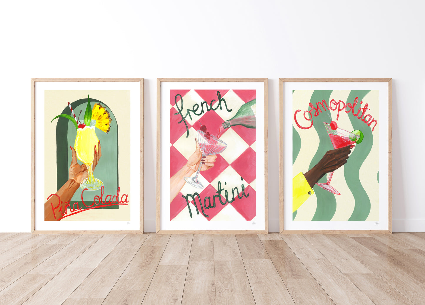 Three framed cocktail posters on a wall with a wooden floor.