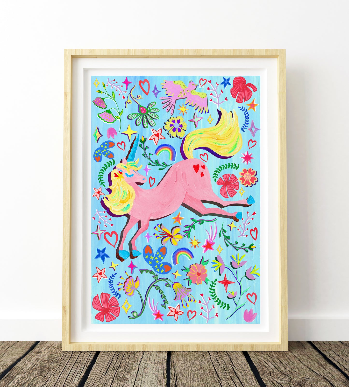 colourful pink uncorn on a sky blue background surround by flower, star and heart rainbow illustrations in a light wood frame