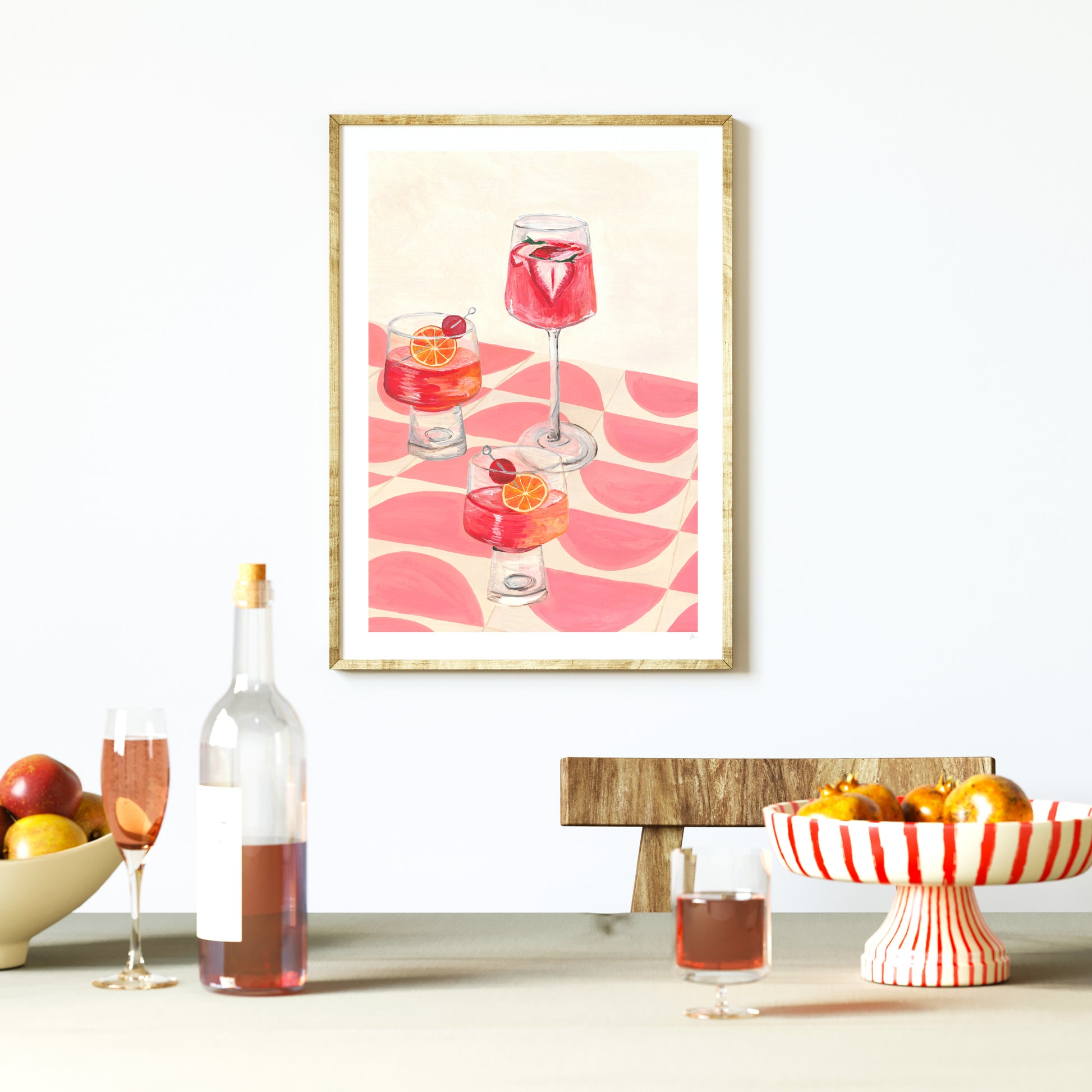 Framed artwork of cocktails on a wall with a table setup featuring drinks and fruit.