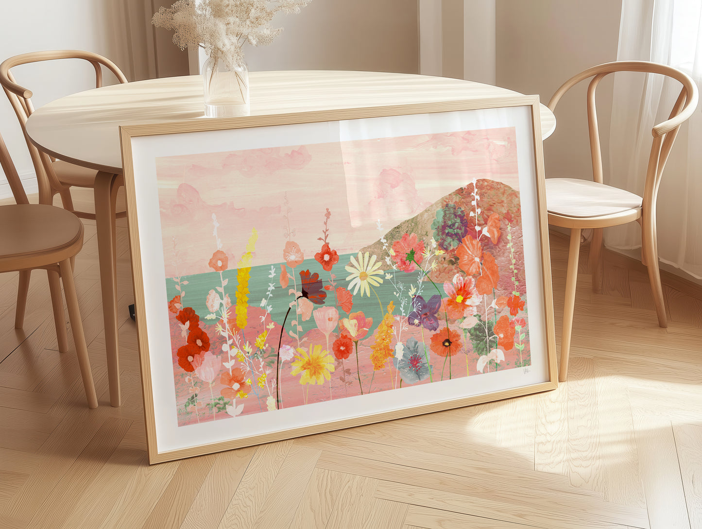 Framed floral artwork on a wooden floor with chairs and a table in the background