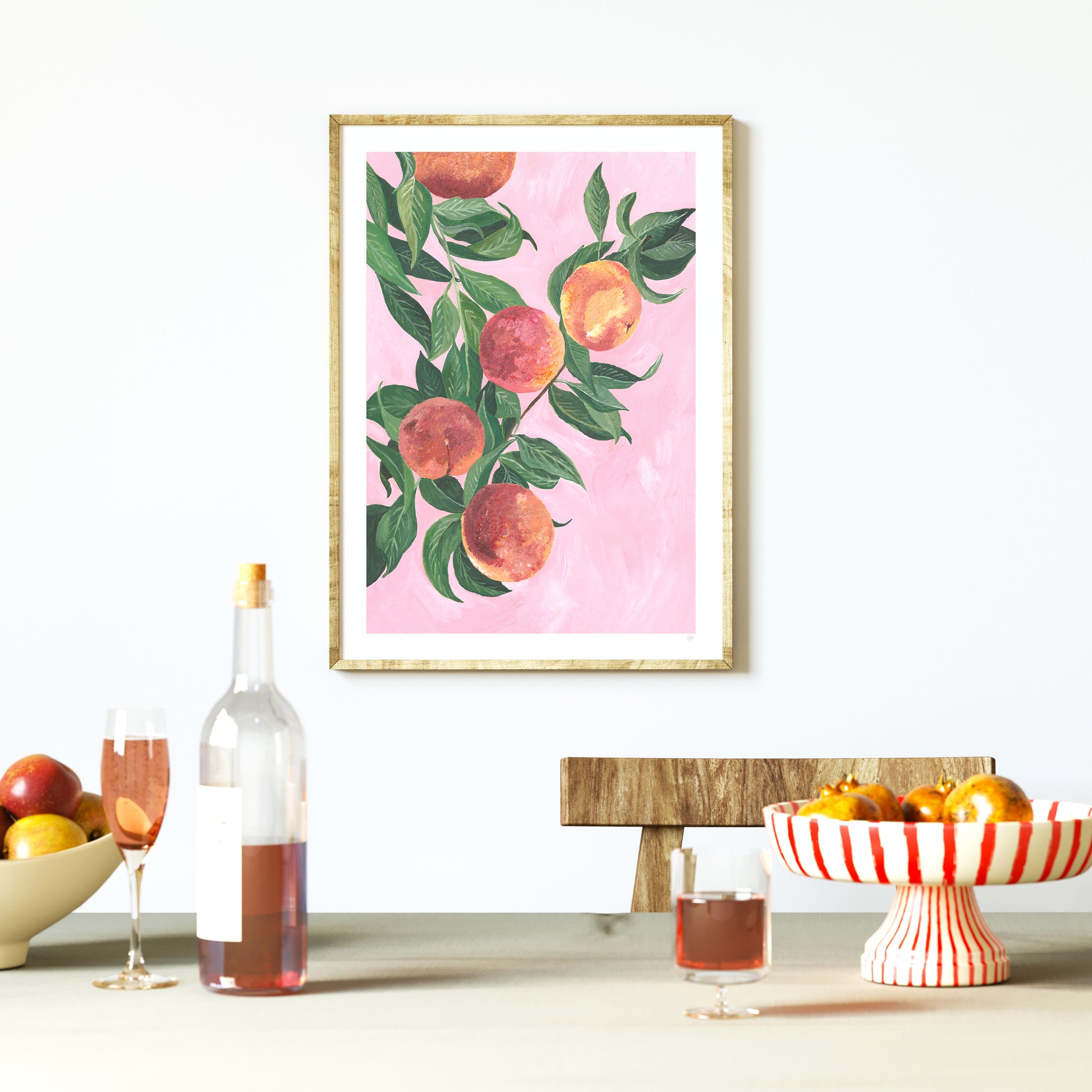 Framed artwork of peaches on a pink background in a room with fruit and wine.