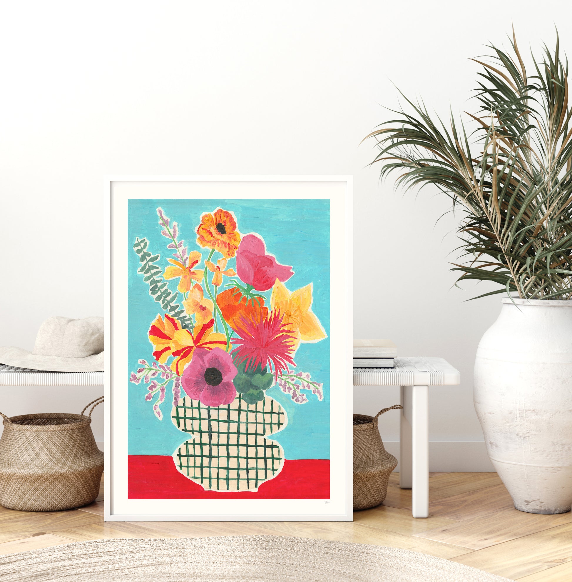 Colorful floral artwork in a white frame on a wall with a plant and decor items below.