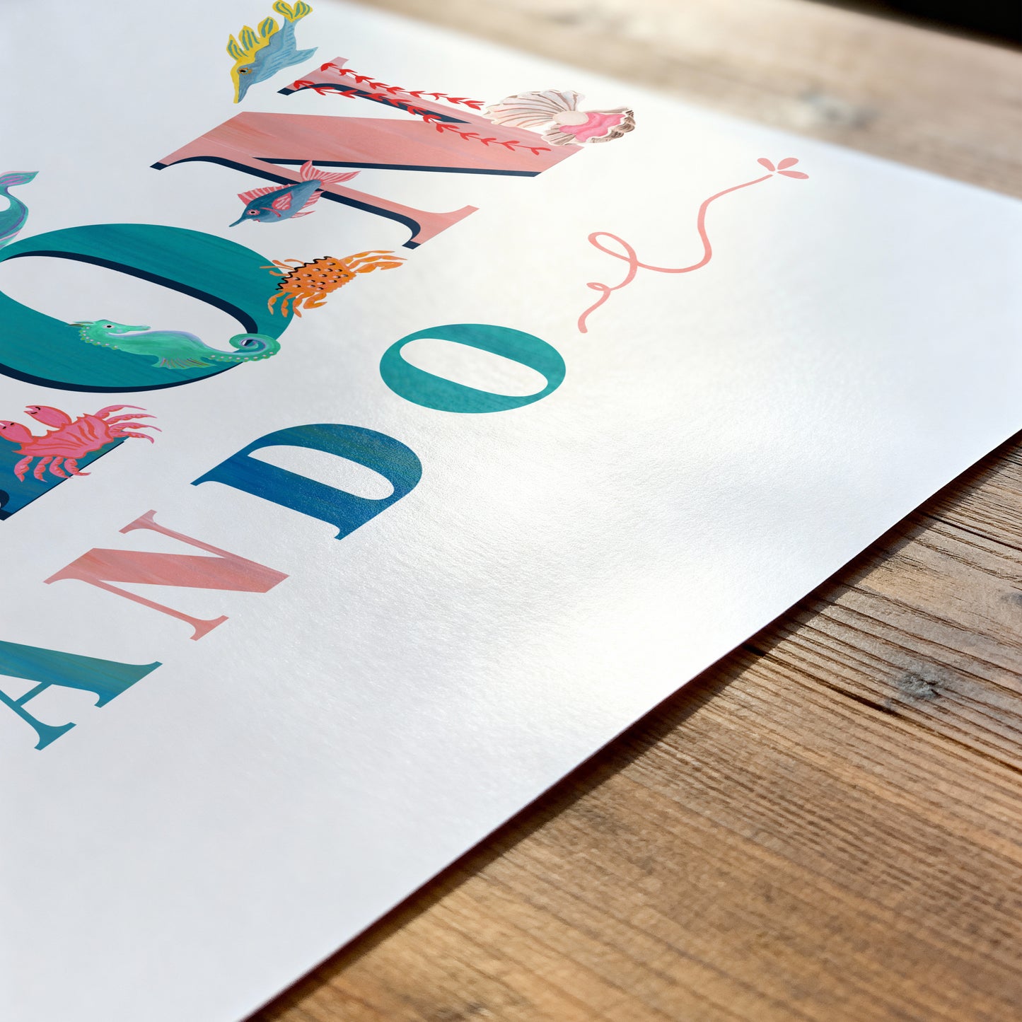 Colorful name print with  sea animal illustrations on a white sheet of paper with a wooden surface underneath