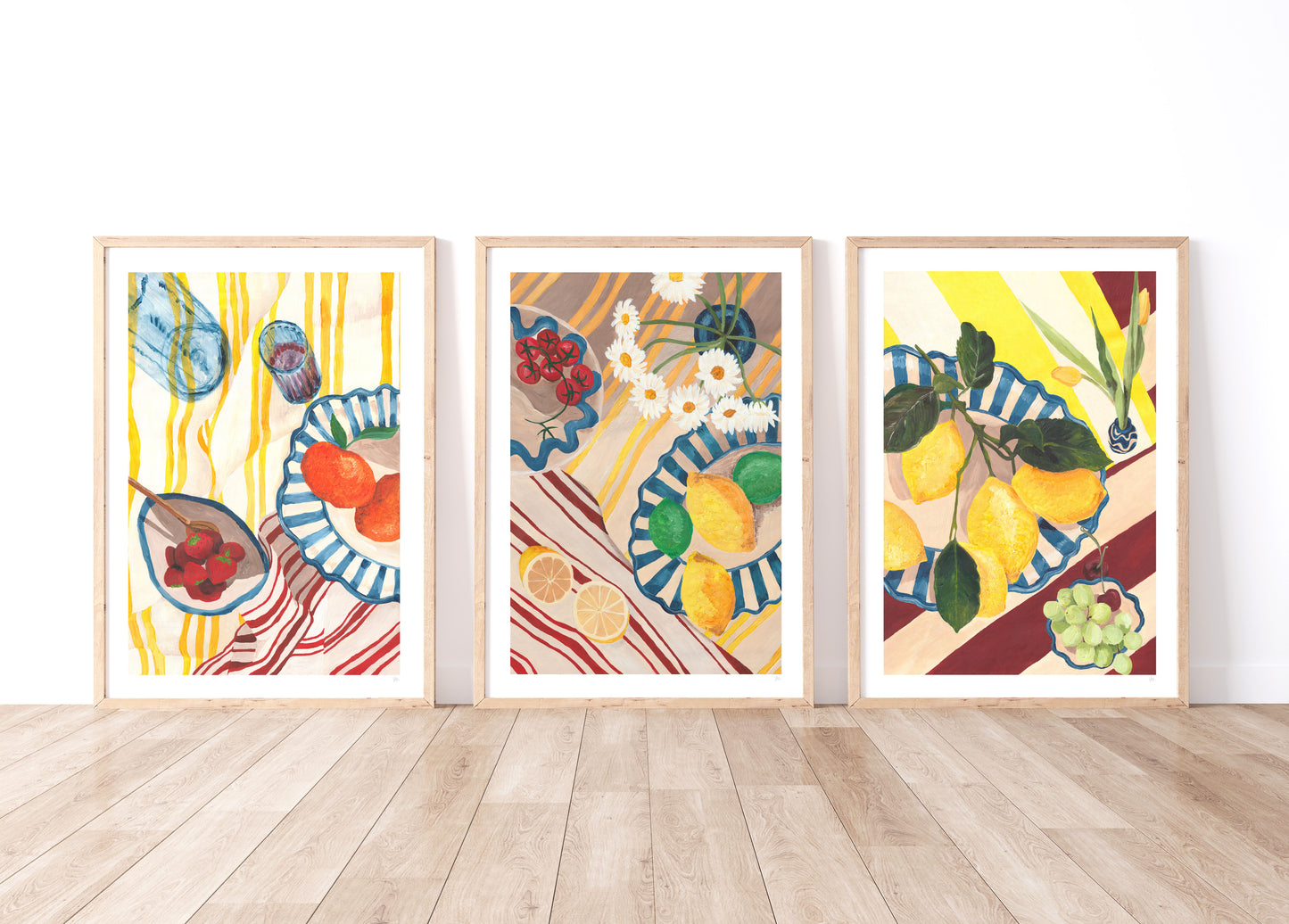 Three framed artworks with colorful fruit and tableware designs on a white wall.
