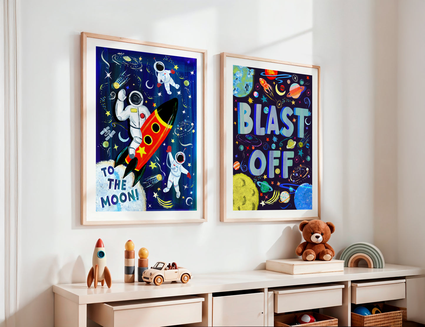 Two framed space-themed posters on a wall above a child's desk with toys.