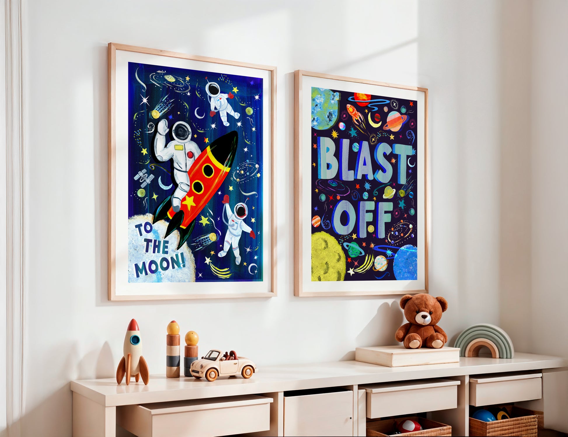 Two framed space-themed posters on a wall above a child's desk with toys.