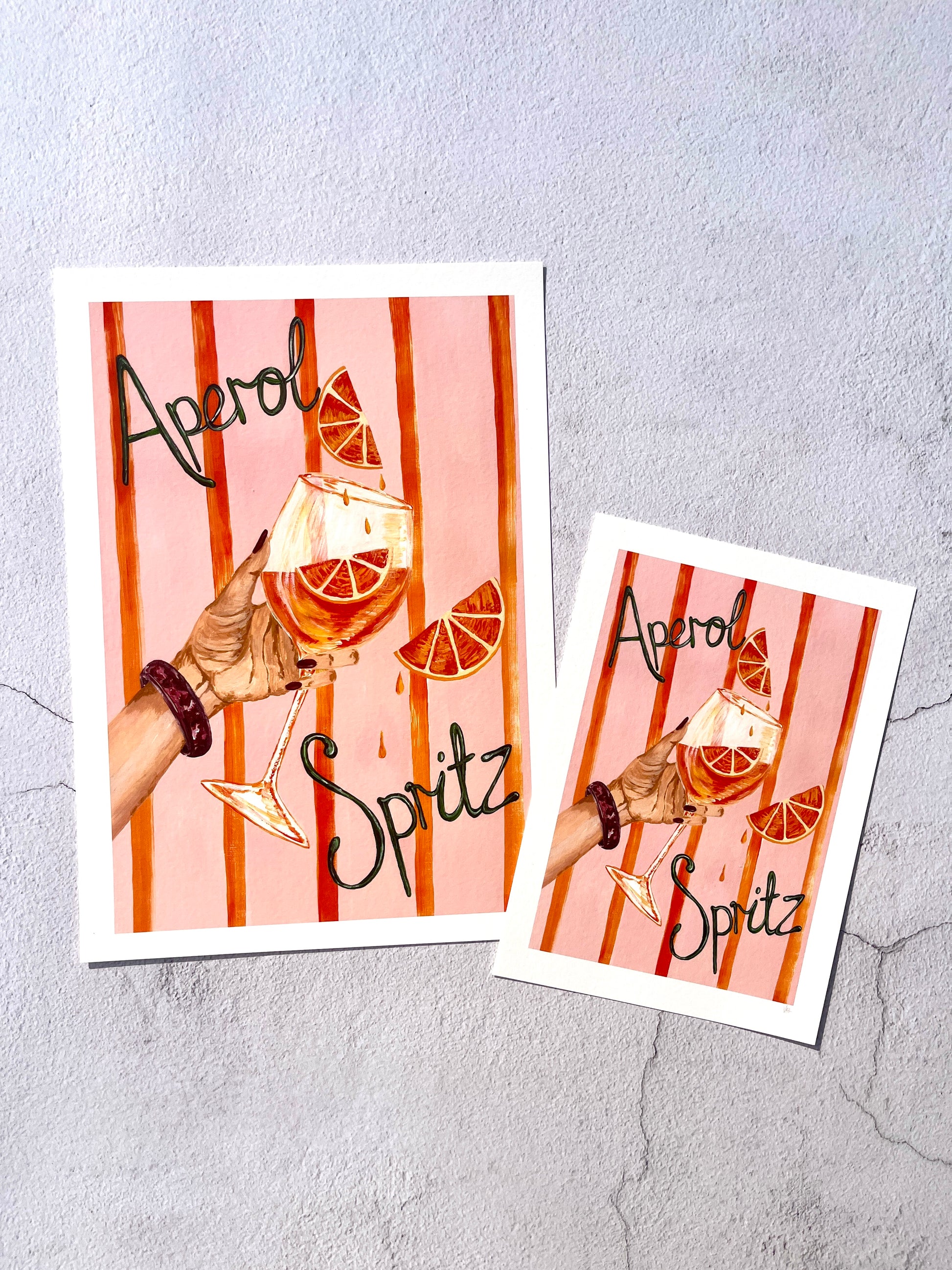 Two Aperol Spritz-themed posters on a textured gray surface.