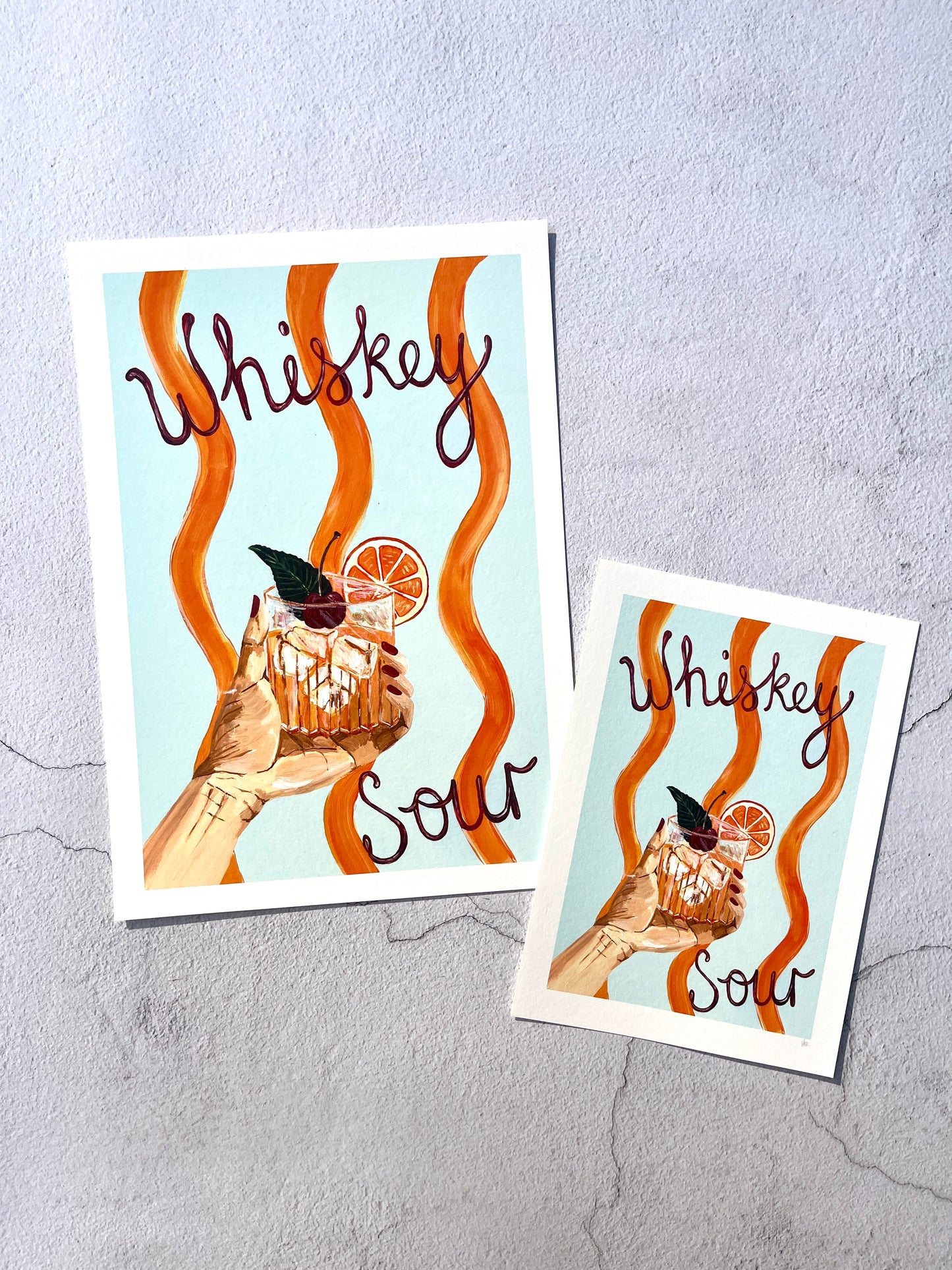 Two prints with illustrations of a cocktail glass and the text 'Whiskey Sour' on a textured gray background.