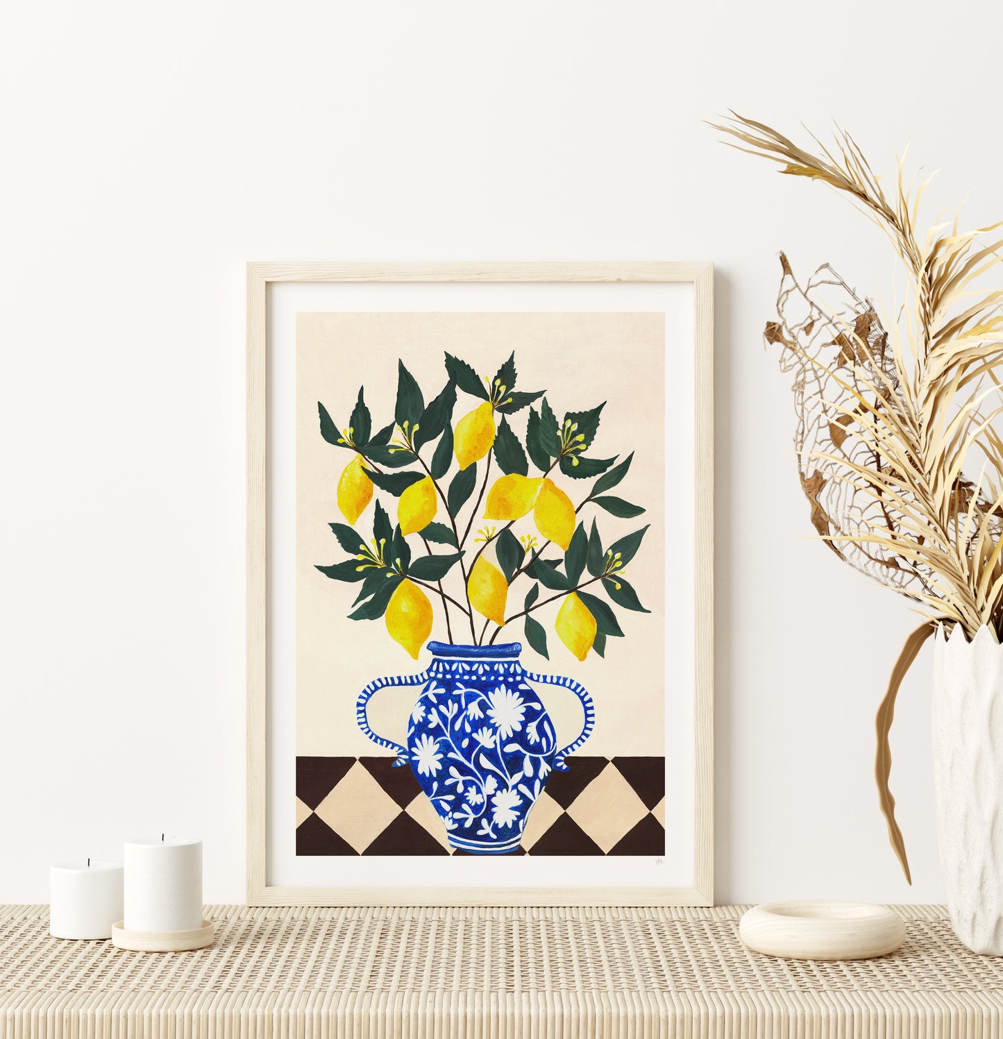 Framed artwork of lemons in a blue vase on a table with decorative elements.