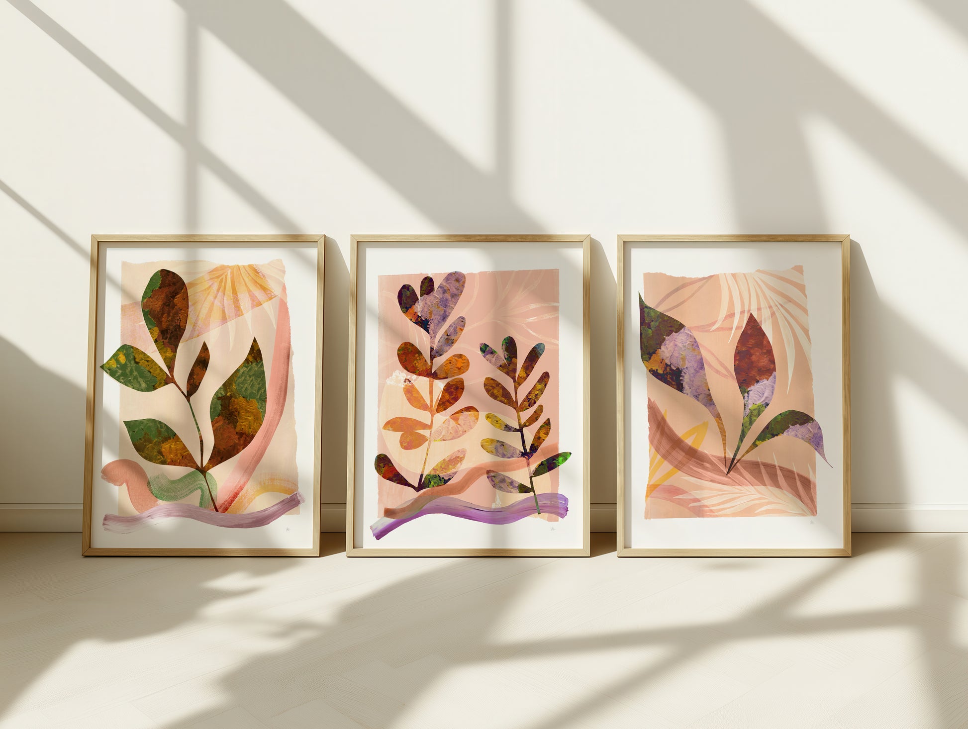 Three framed abstract art pieces on a wall with sunlight casting shadows.
